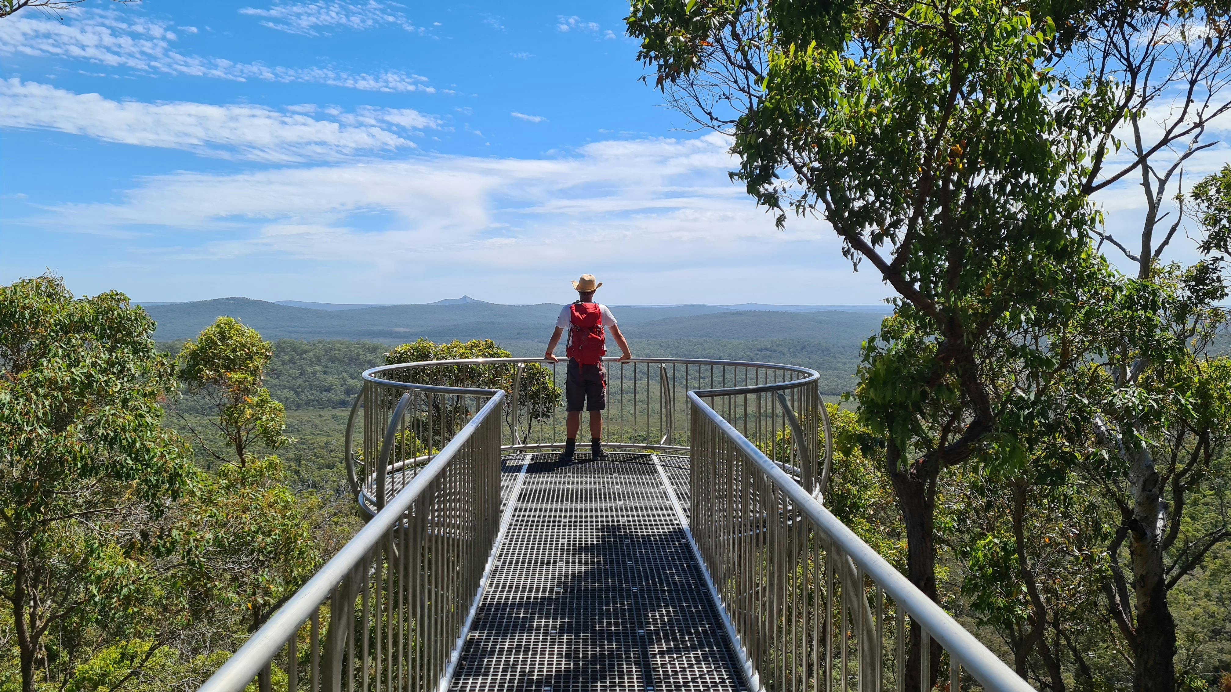 Man standing at the end of a high lookout looking away at the views of a vast Australian landscape