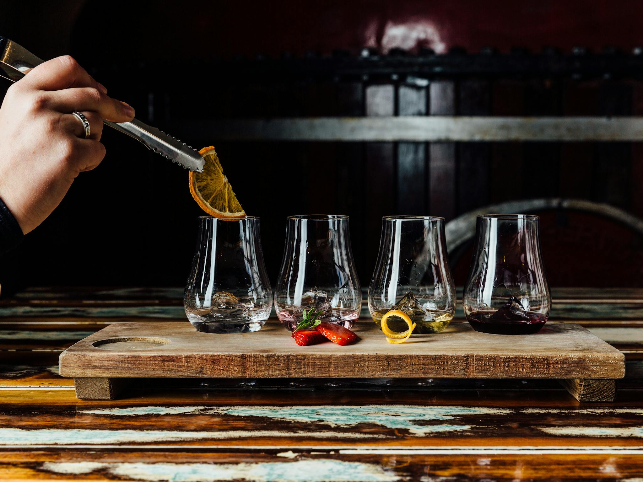 Gin tasting paddle with someone placing a garnish into one of the glasses.