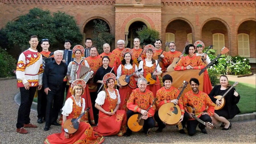 Members of the orchestra posing together in front of a building, some holding instruments