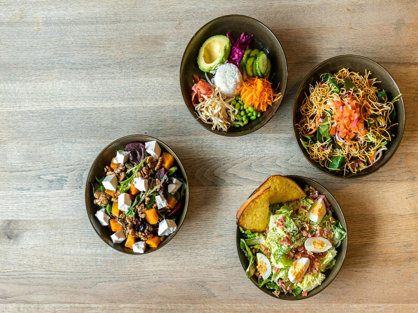 Four fresh and colourful salads on a wooden table