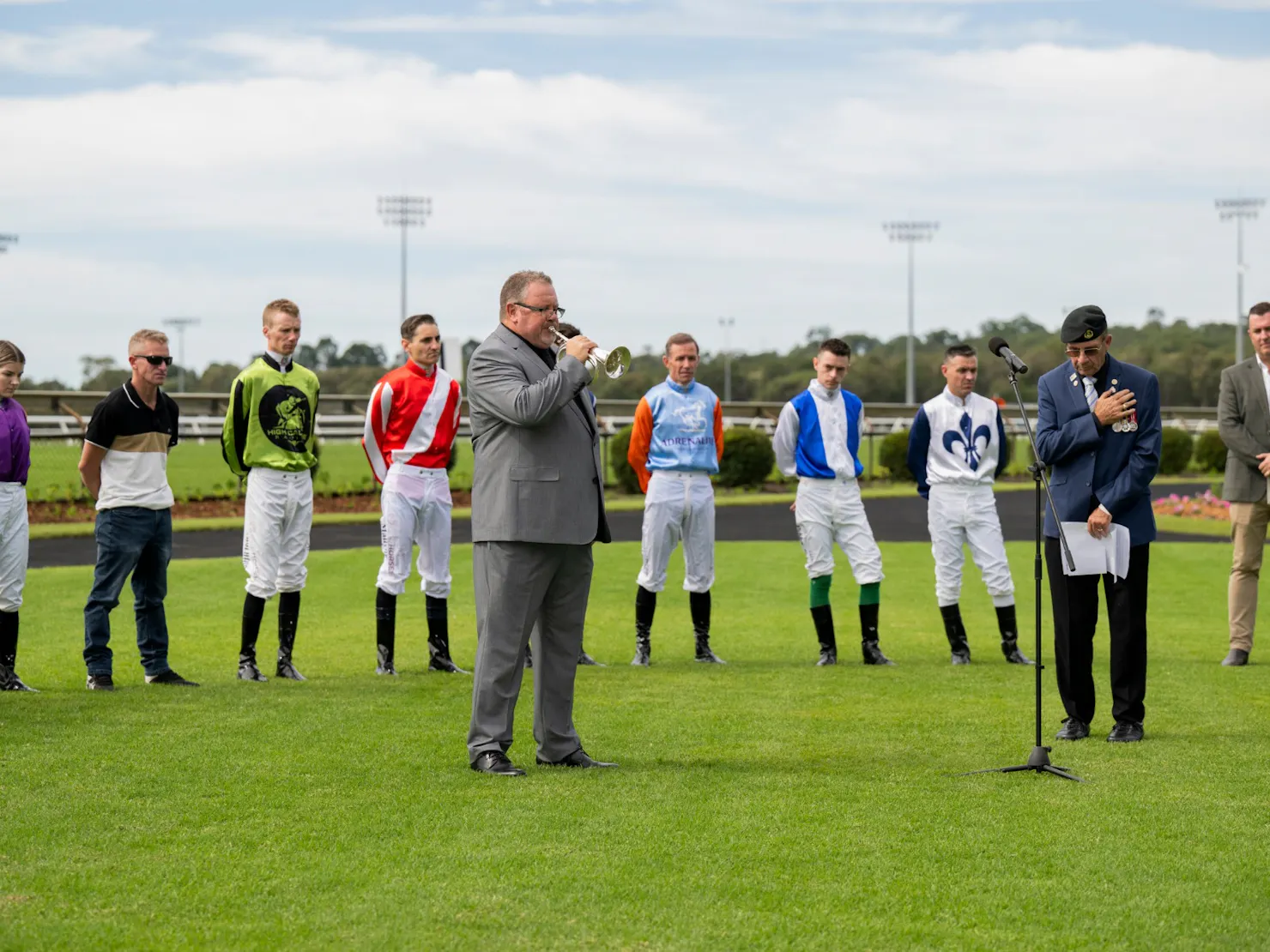 Jockeys in silks and man playing the trumpet paying tribute to  the fallen soldiers