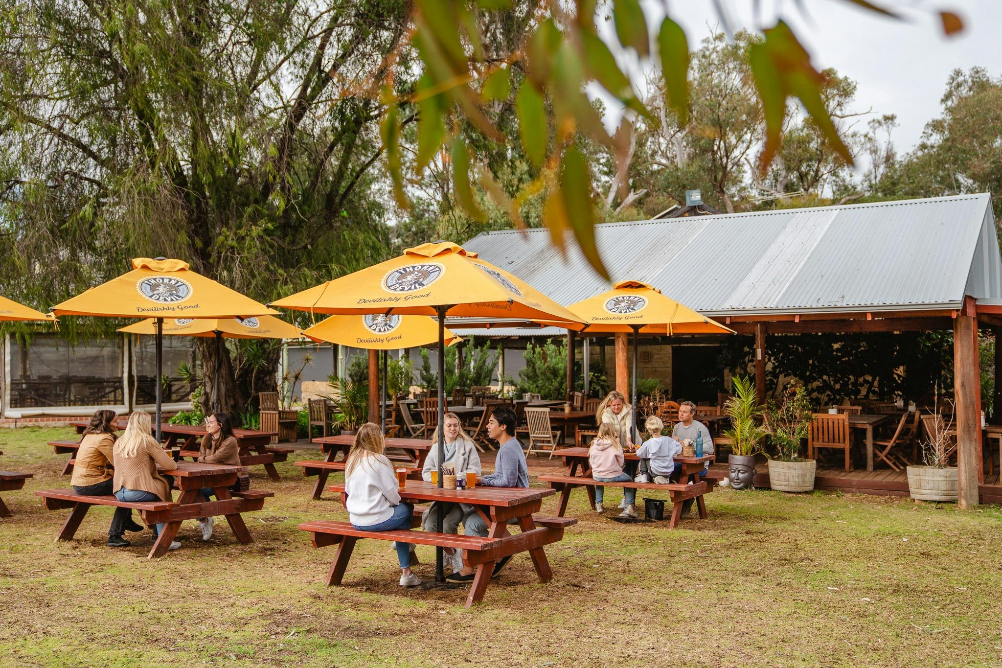 A wide shot of a beer garden with people sat around tables drinking beer and eating lunch.