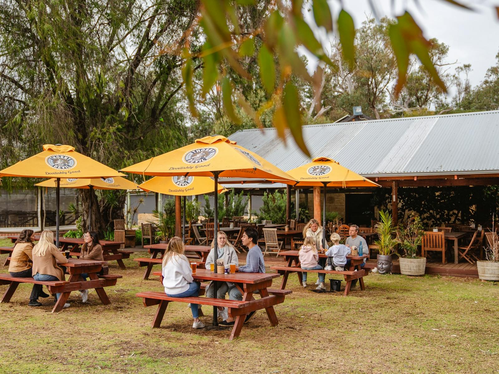 A wide shot of a beer garden with people sat around tables drinking beer and eating lunch.