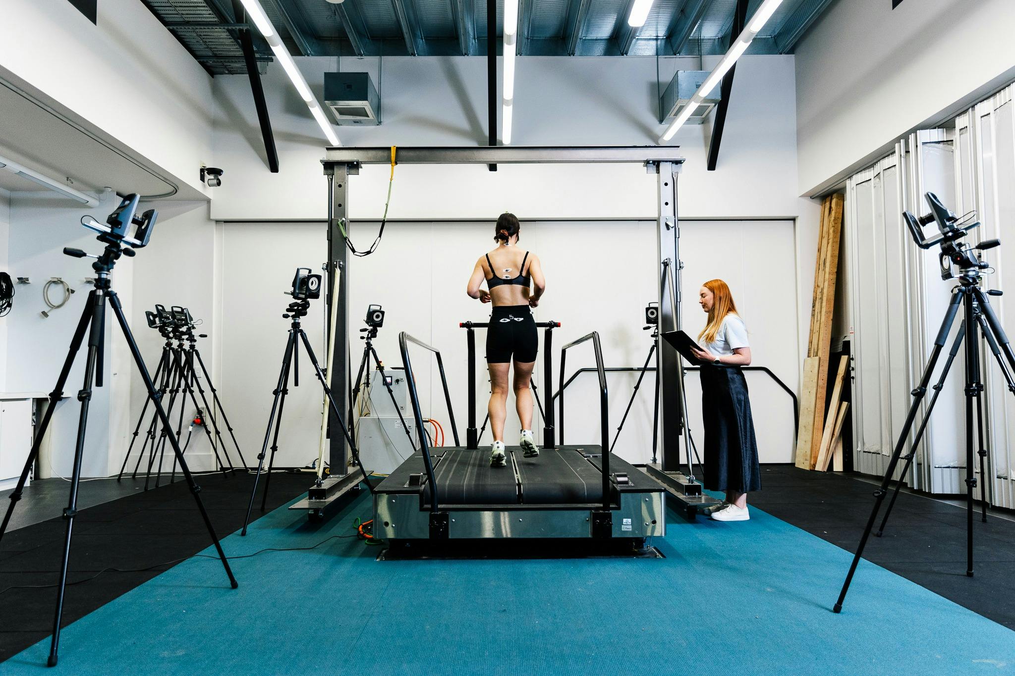 A woman in active wear runs on a treadmill for biomechanics testing with a researcher observing.