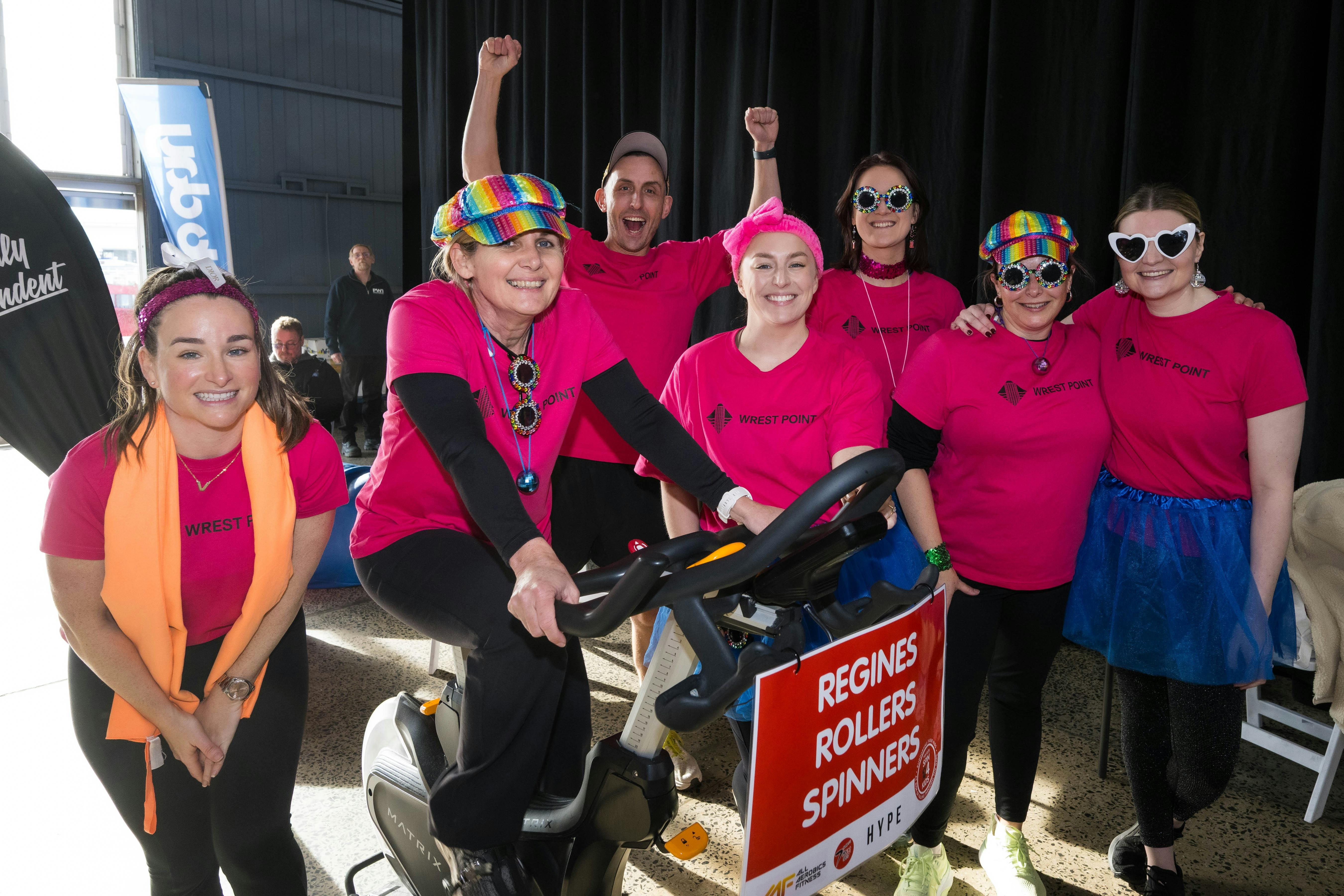 Regines Rollers team in pink t-shirts and fun heart sunglasses on a spin bike at Variety Spin4Kids