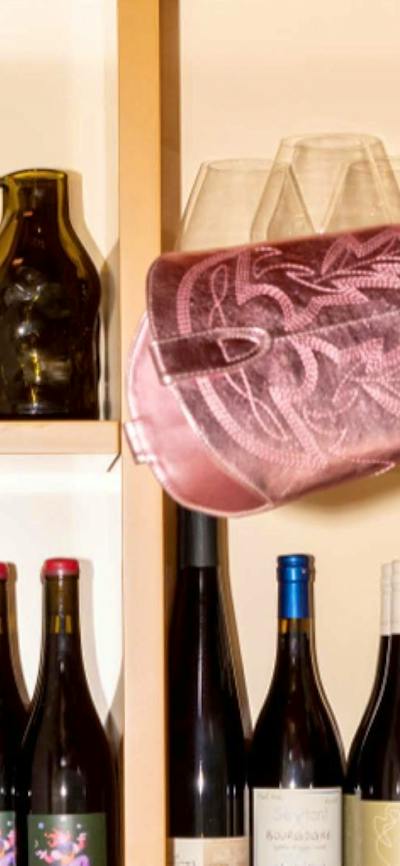 A metallic pink cowboy boot sits at a peculiar angle on a shelf full of wine