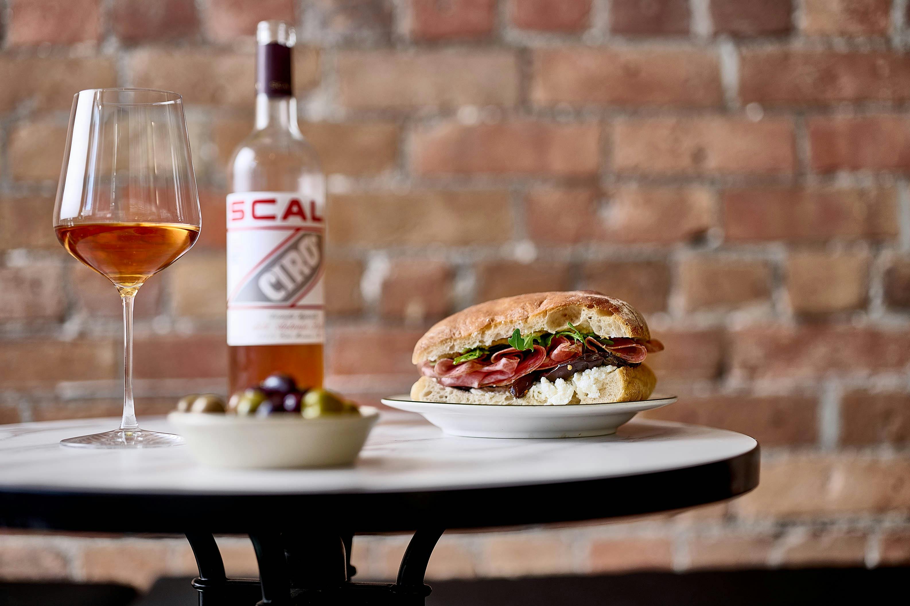 Italian panini, glass of wine and wine bottle and bowl of olives