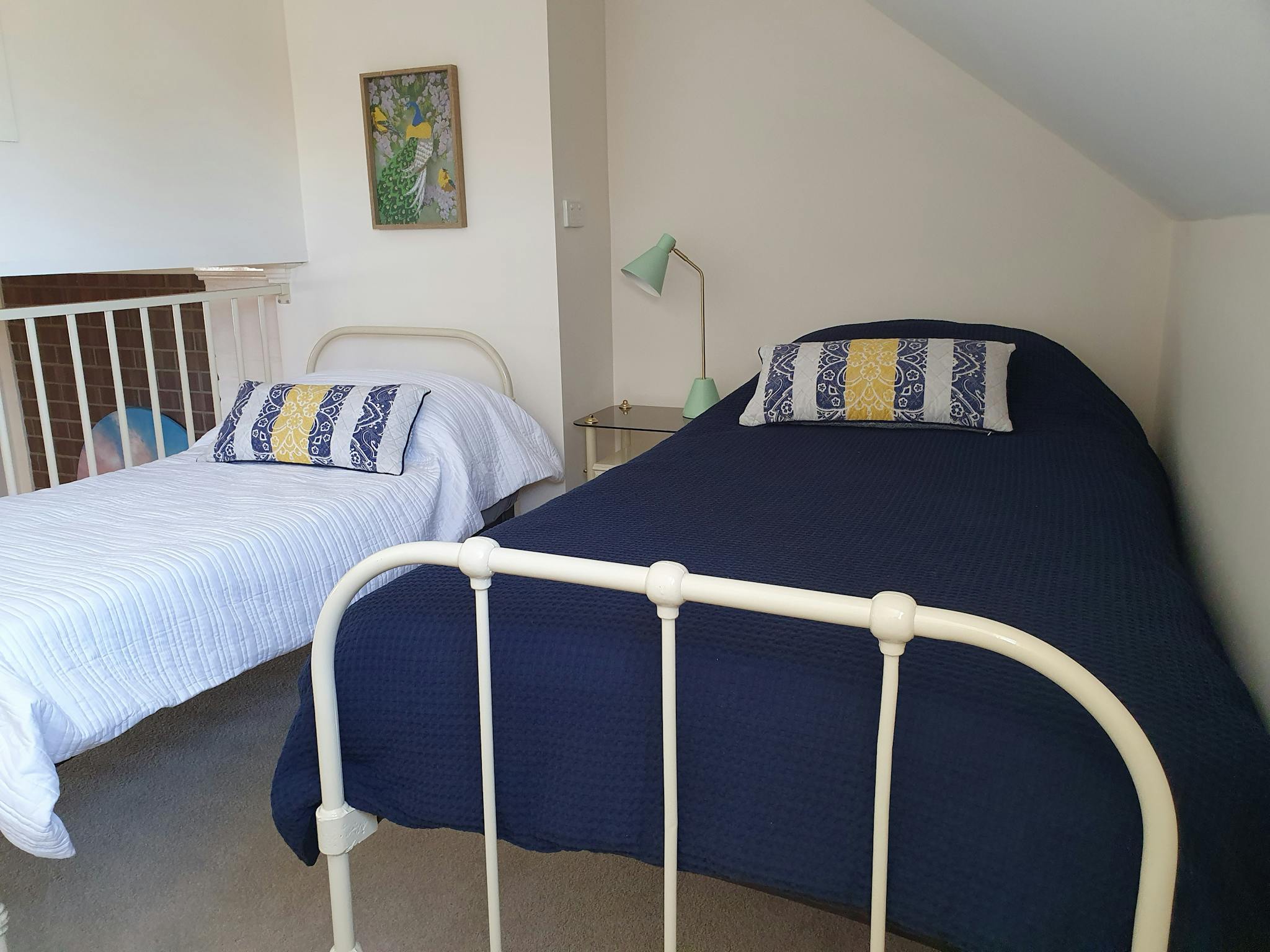 Two single beds beautifully made with blue covers and pillows in a upstairs bedroom.