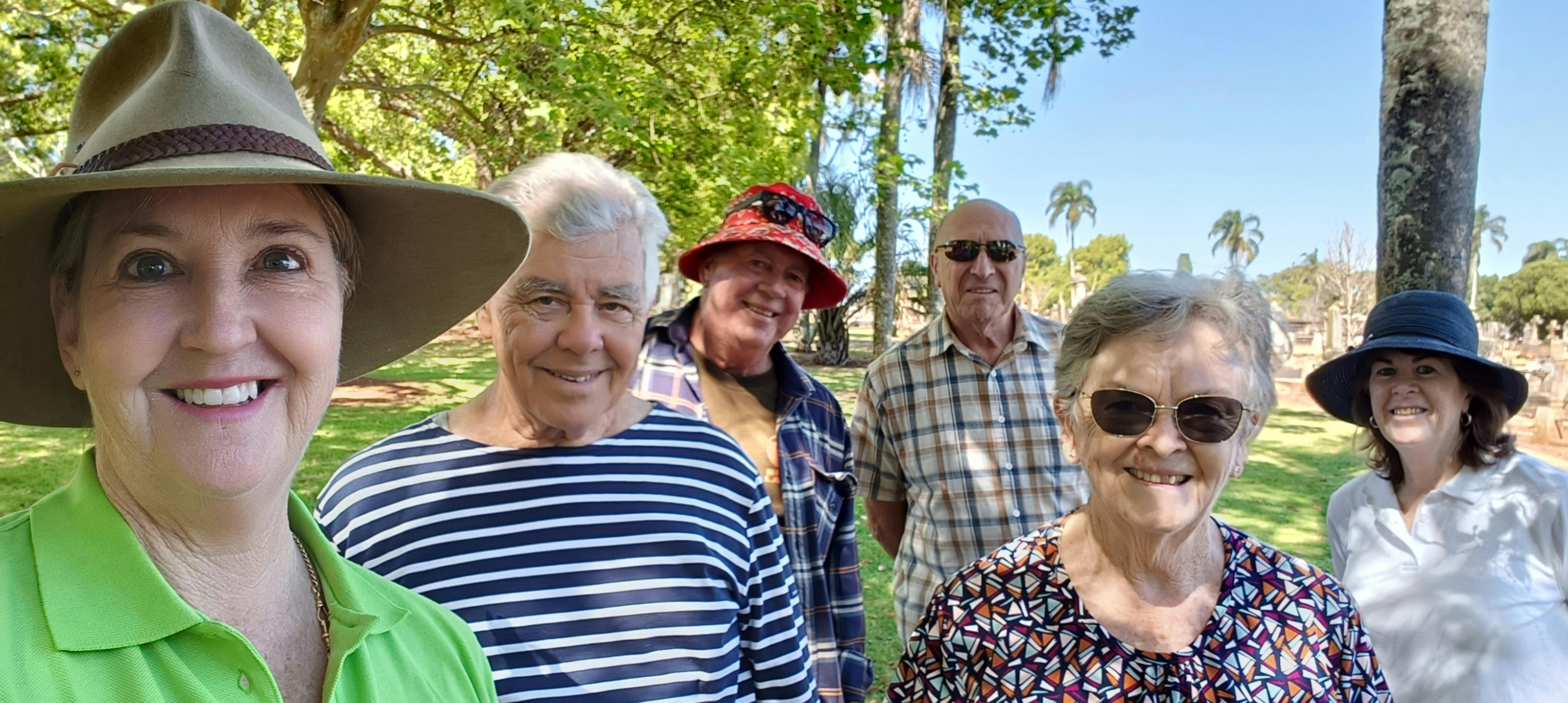 Six people smiling at the camera after a cemetery tour, the guide wearing a large hat and lime shirt