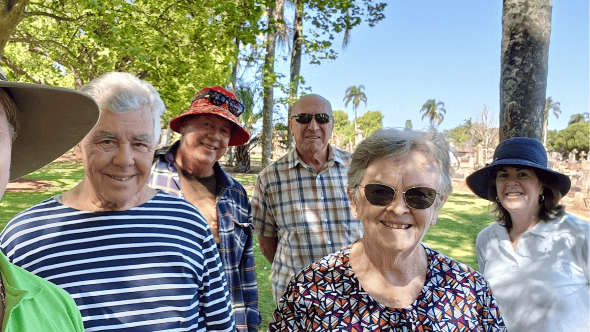Six people smiling at the camera after a cemetery tour, the guide wearing a large hat and lime shirt