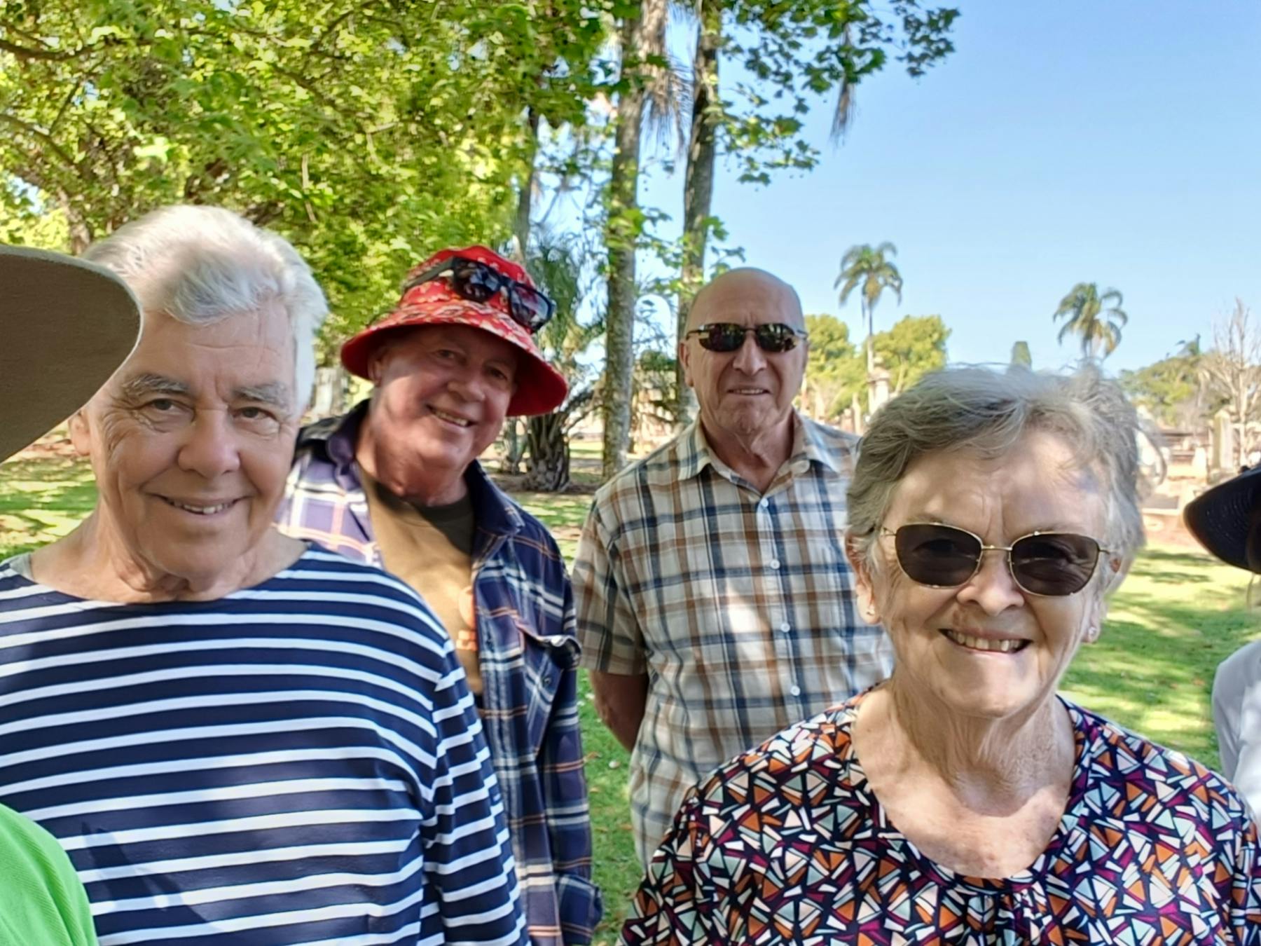 Six people smiling at the camera after a cemetery tour, the guide wearing a large hat and lime shirt