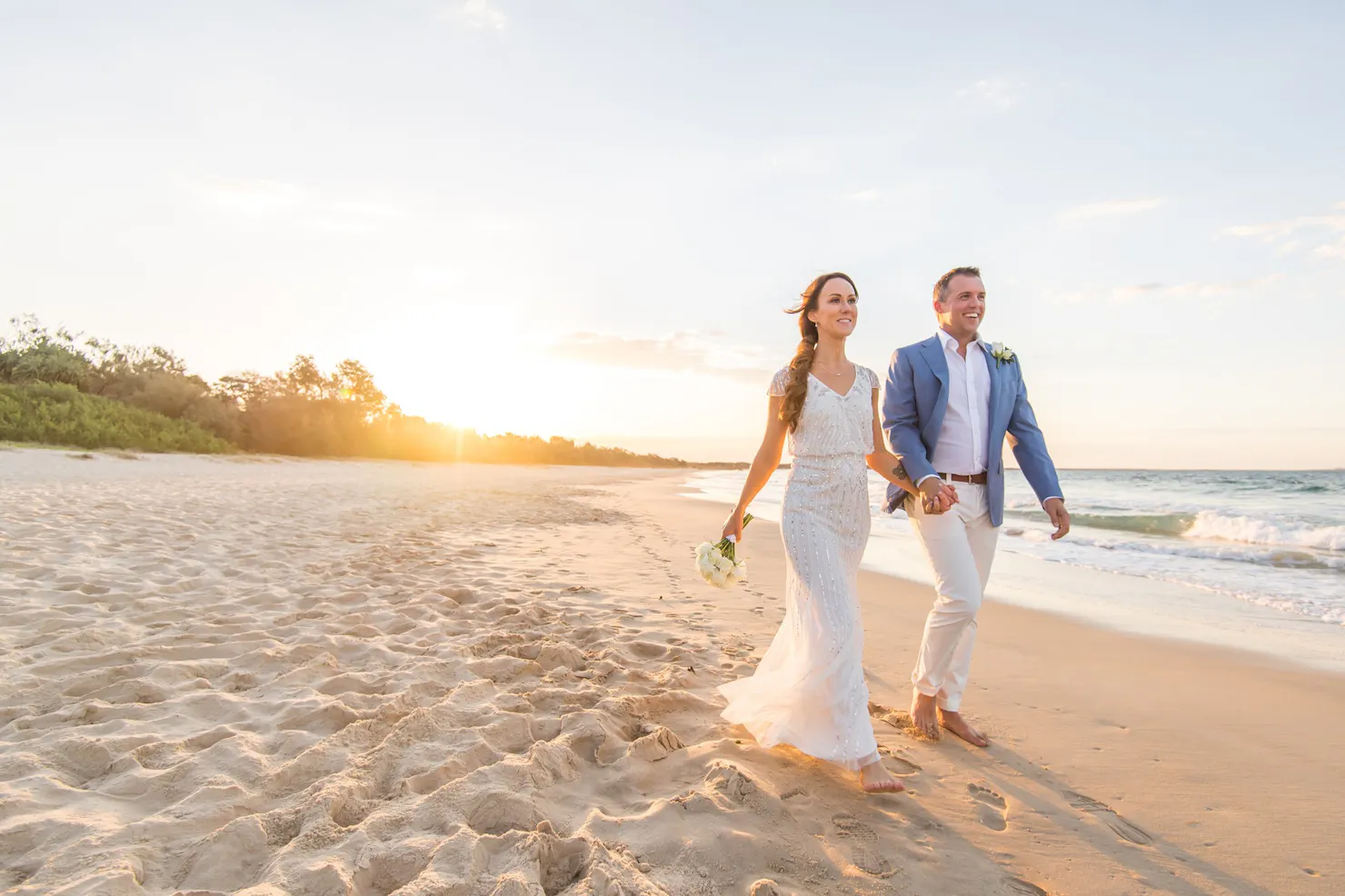 A newly married couple strolling at sunset on Noosa Beach