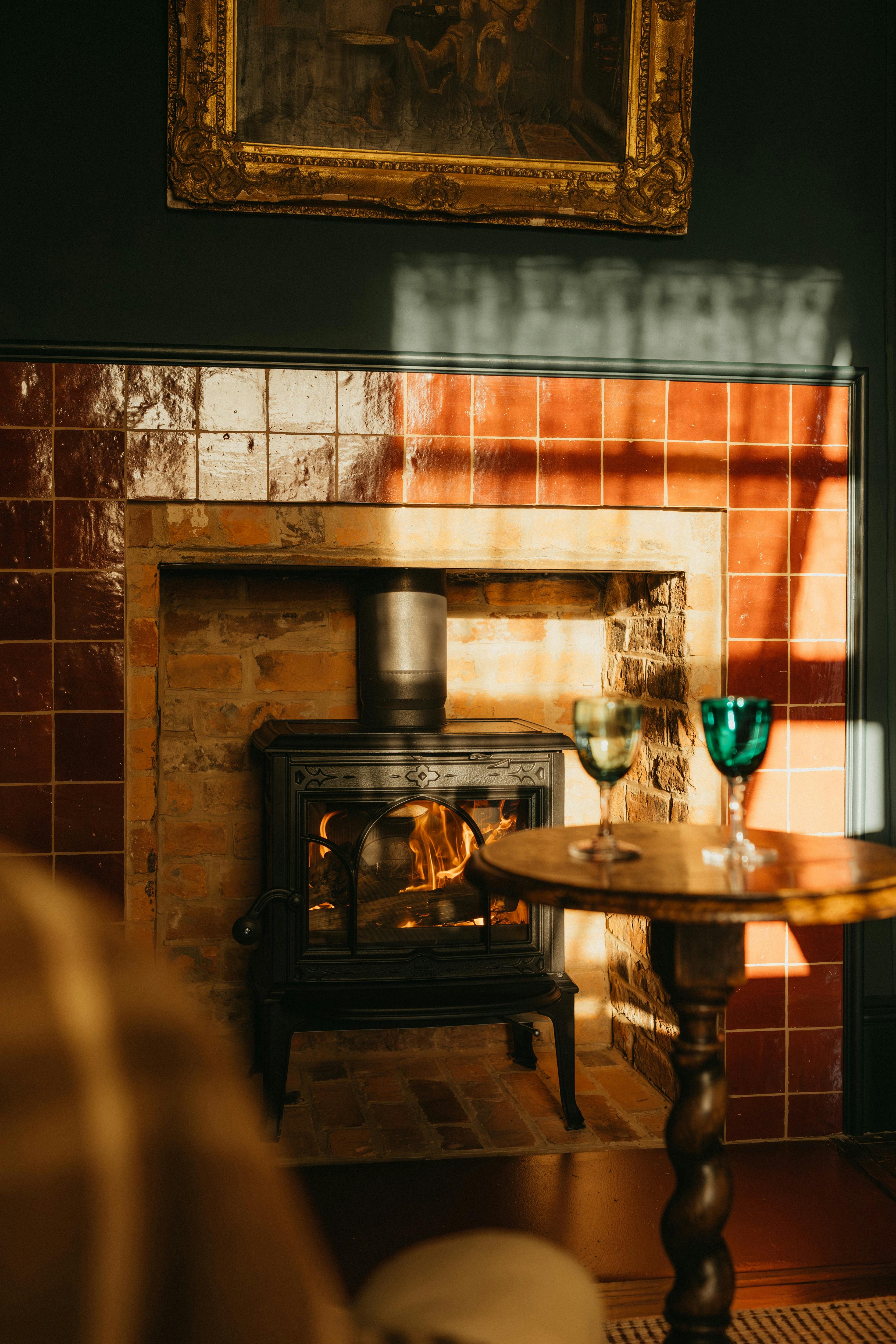 Wood fire in tiled hearth with wine glasses on table in warm glow.
