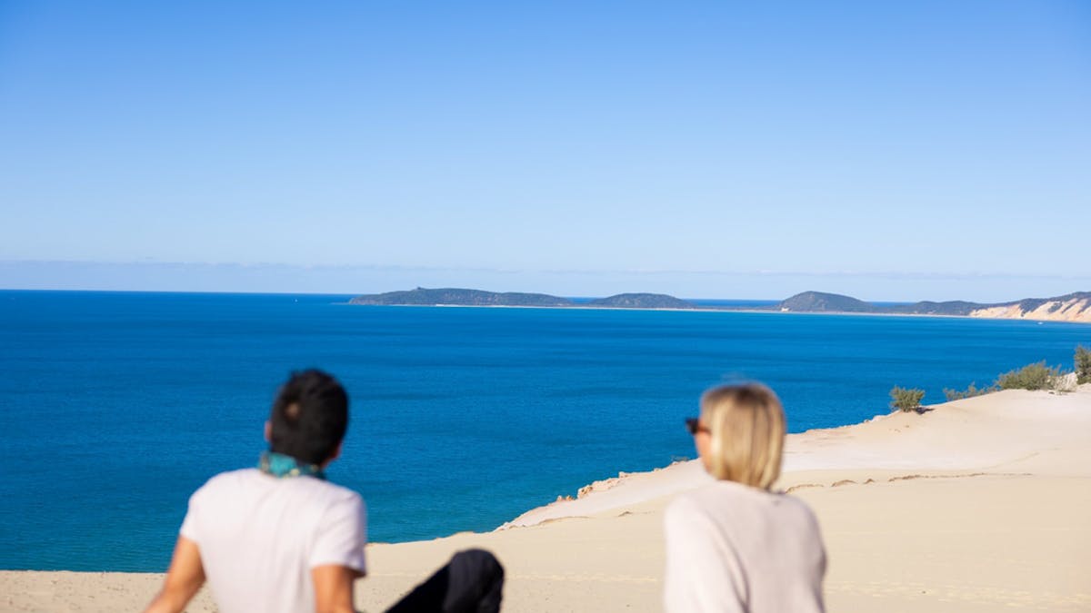 People seating on the sand at Carlo Sandblow looking out at the ocean