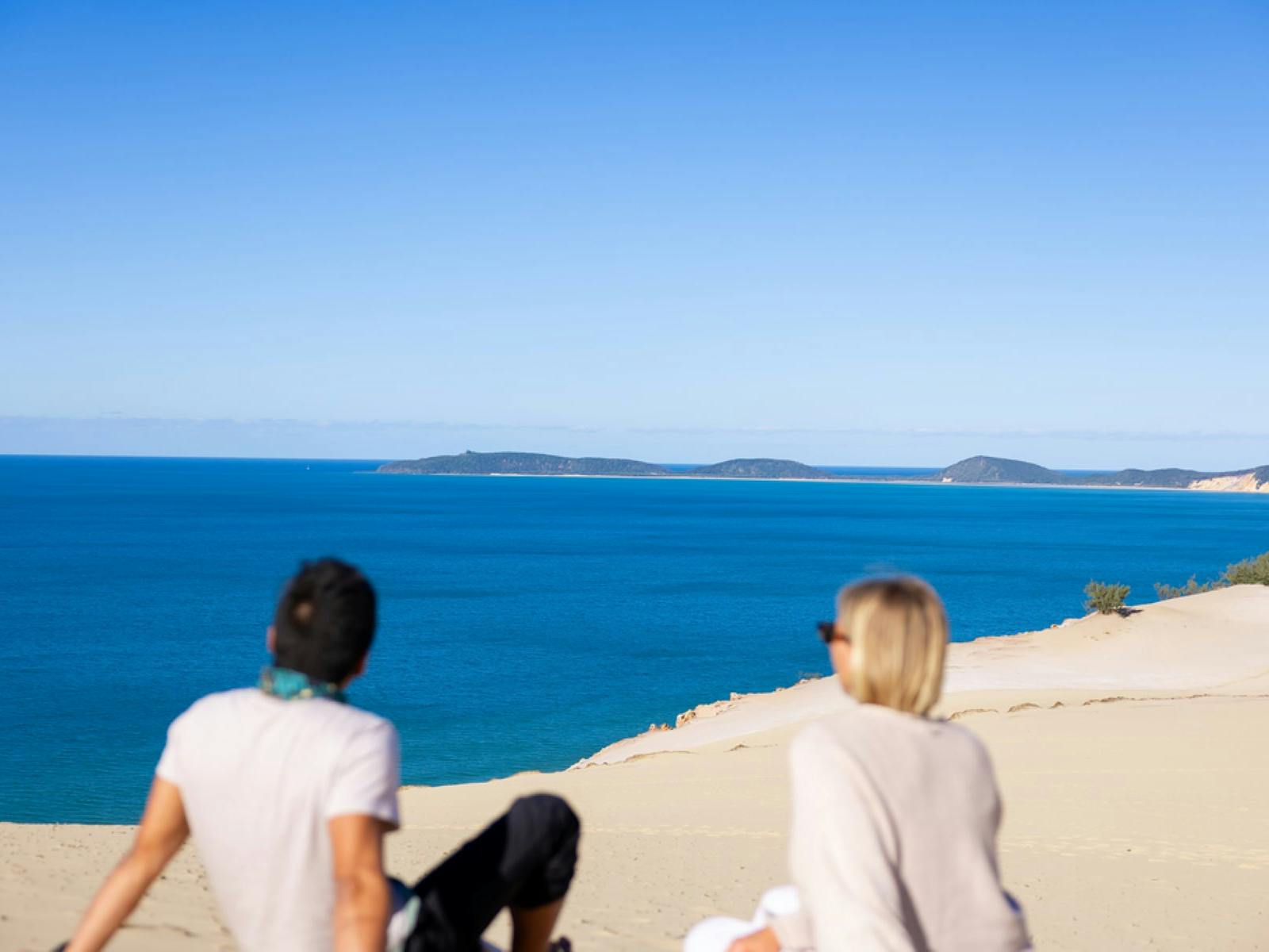People seating on the sand at Carlo Sandblow looking out at the ocean