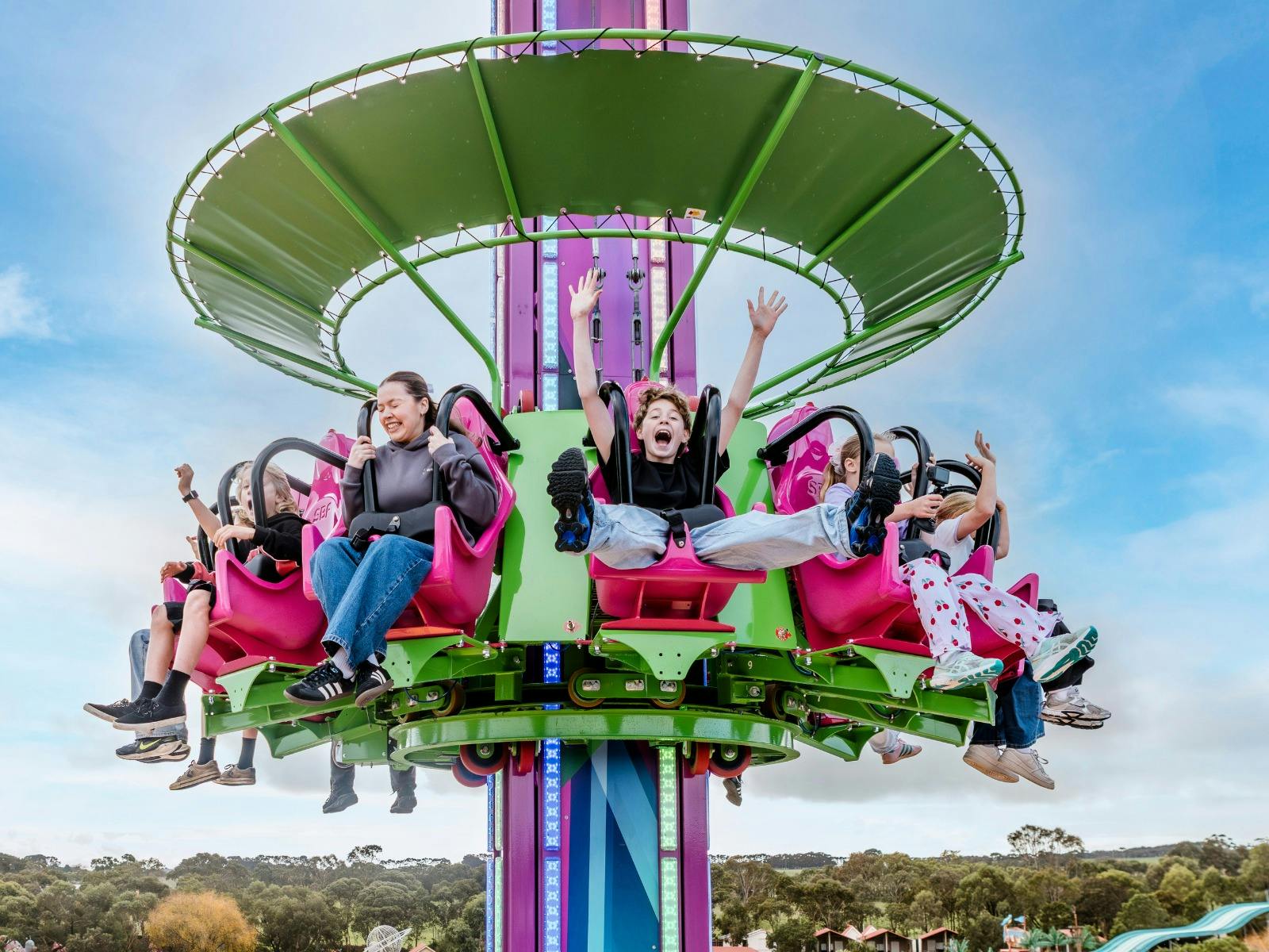 A tall pink drop tower with excited teenagers and adults riding