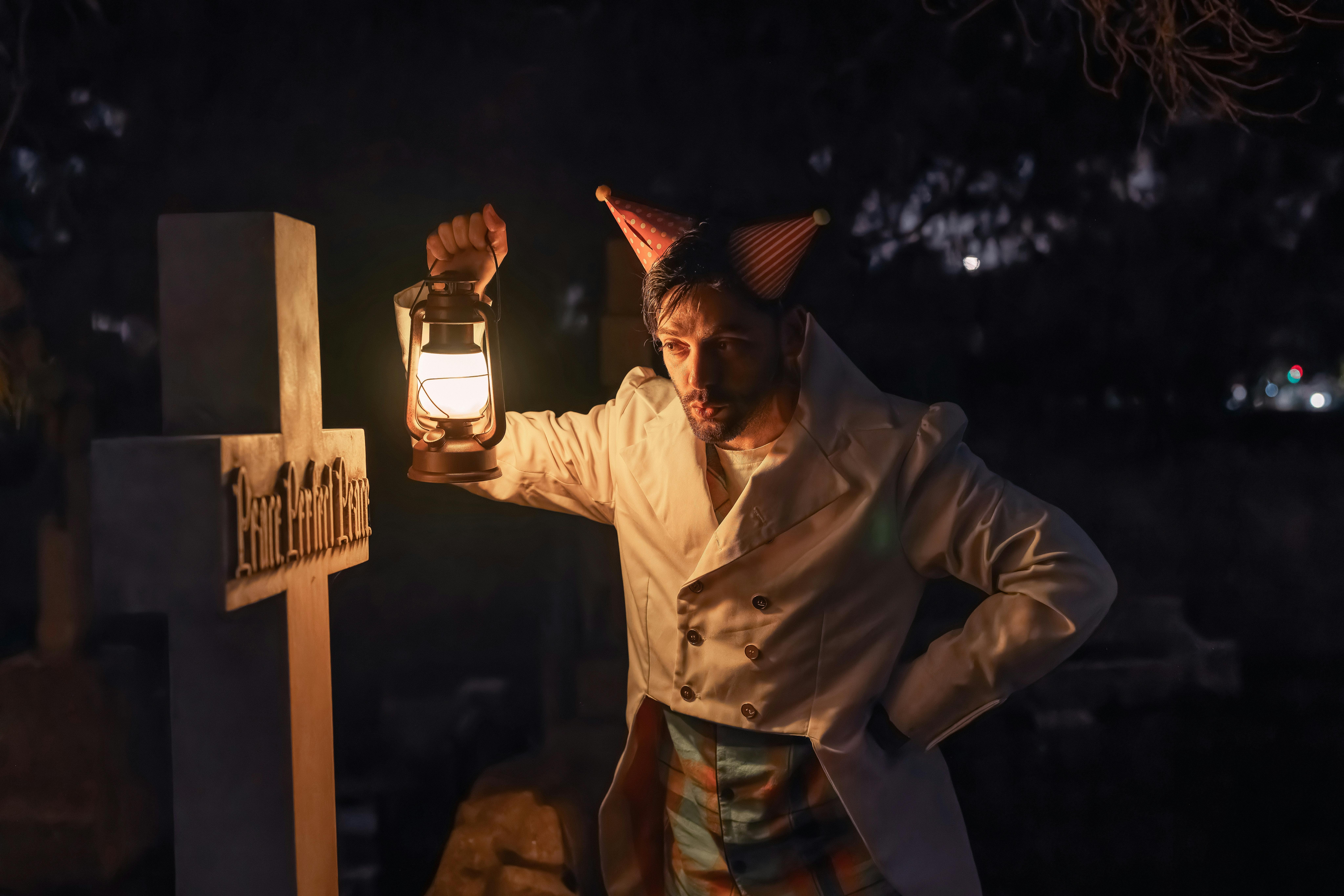 Person in costume holding up a lantern to a grave