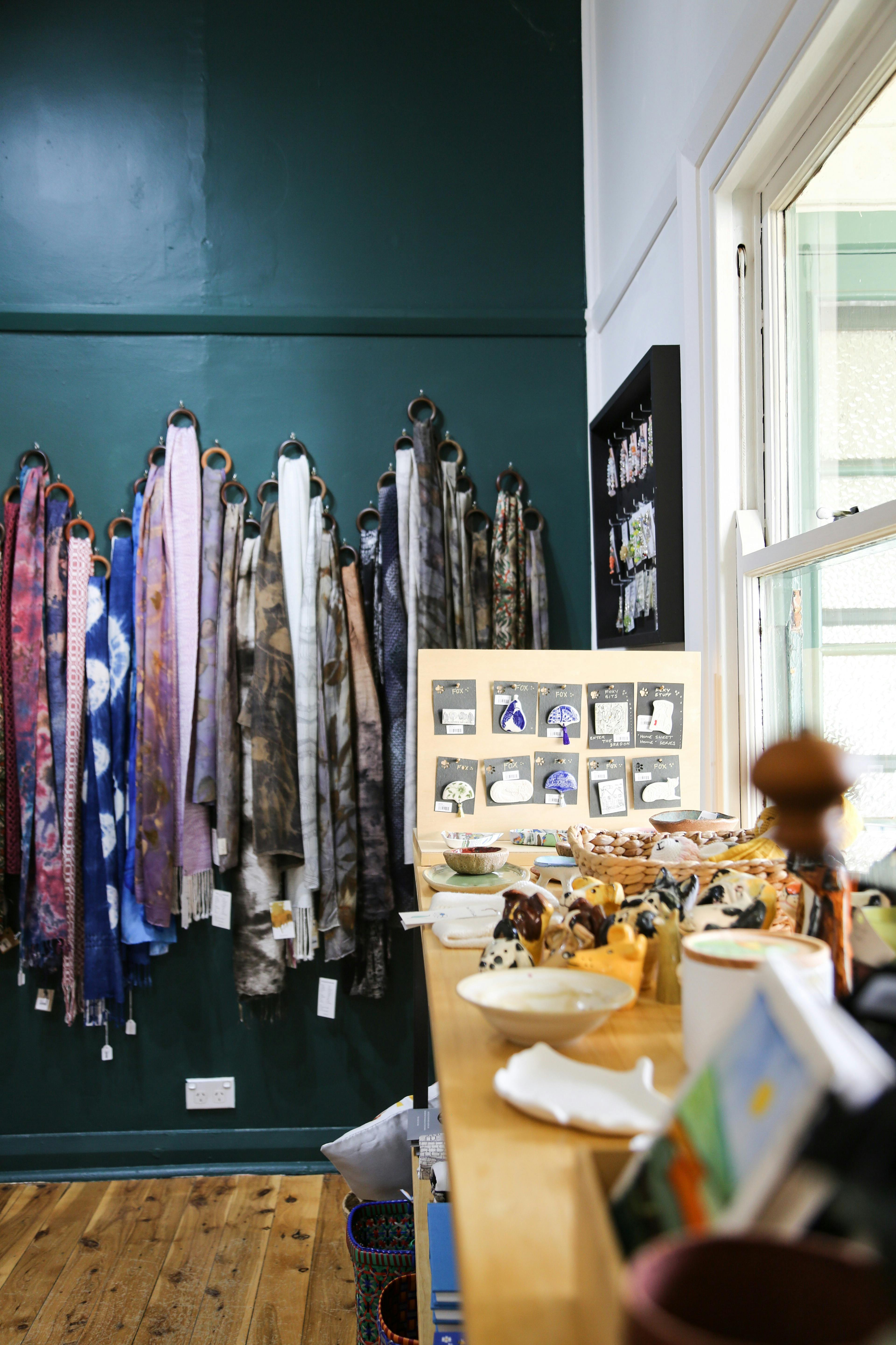 Scarves hang on a green wall behind a display table with jewellery.