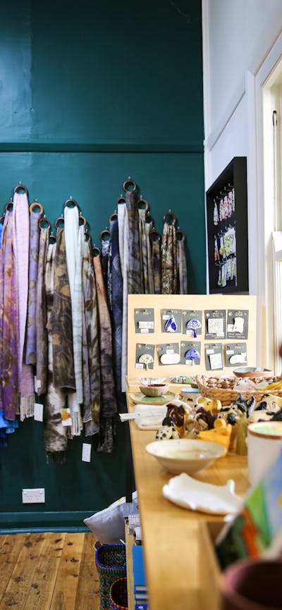 Scarves hang on a green wall behind a display table with jewellery.