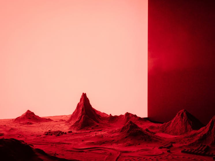 An artwork of a sci-fi landscape made out of sand and wood with a red light backdrop