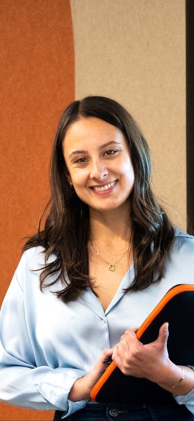 woman smiling at camera holding a folder in an office