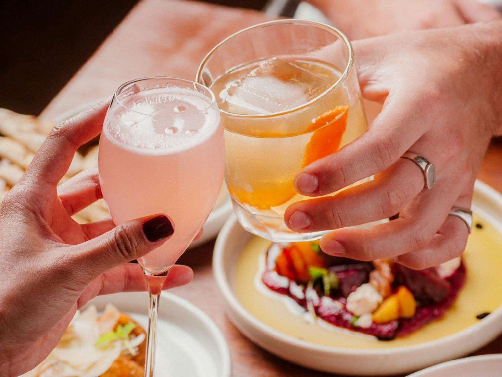 A couple cheers their glasses over a colourful table of food