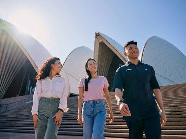 Two women and a male tour guide walking down the steps of the Opera House