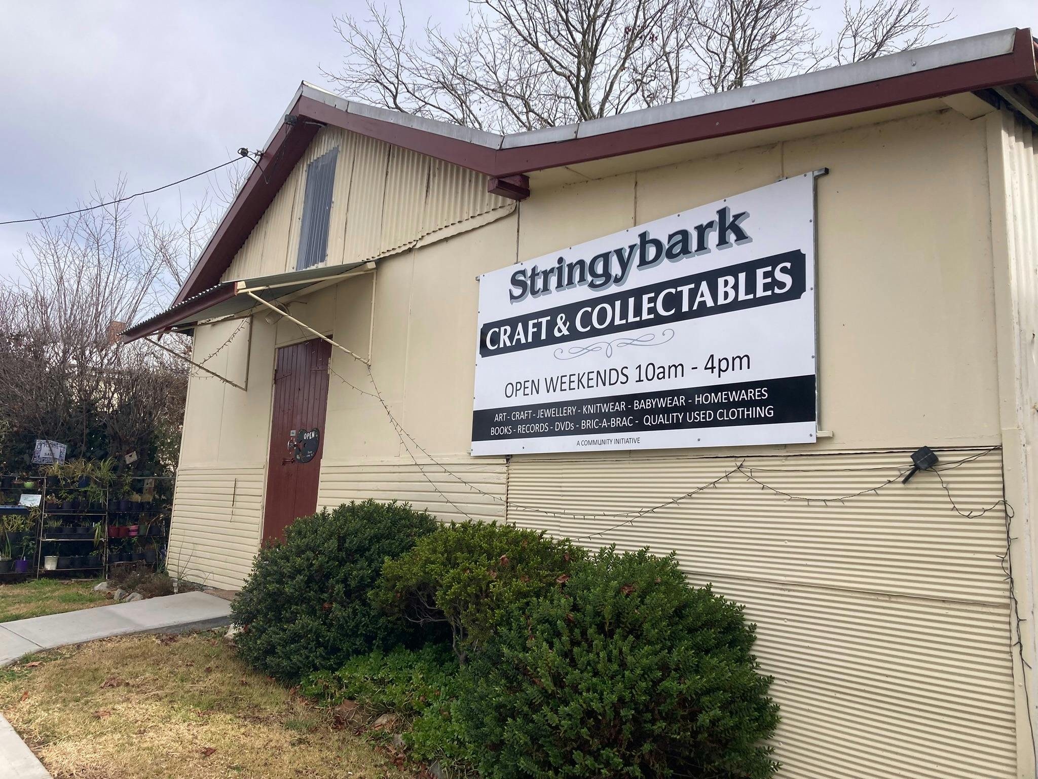 Side angle of cream fibro building with iron roof, red door and new signage