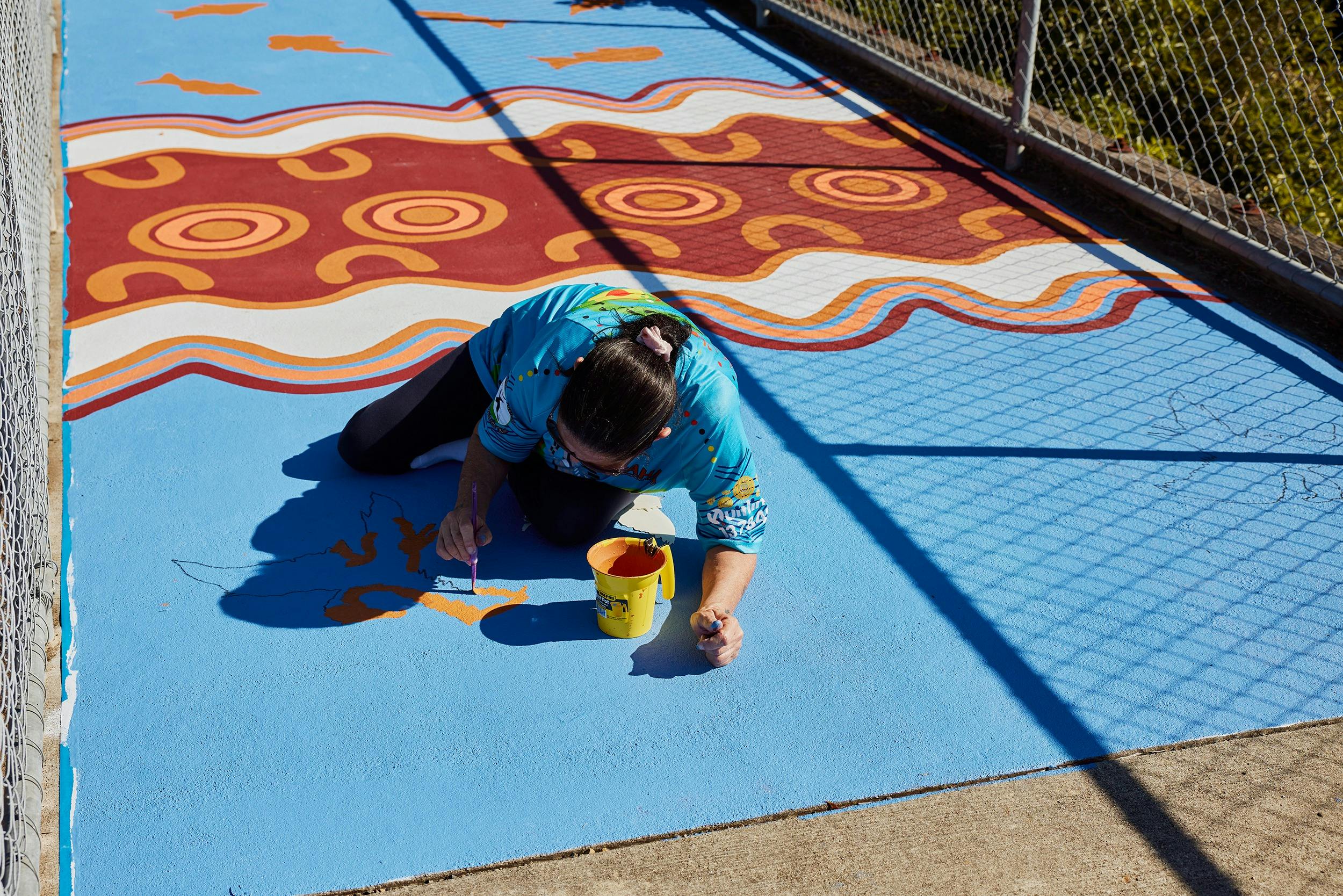 Artist Patricia Pittman painting with orange paint on a blue background on a road