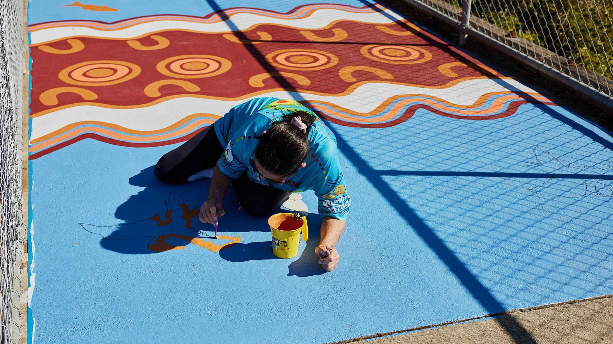 Artist Patricia Pittman painting with orange paint on a blue background on a road