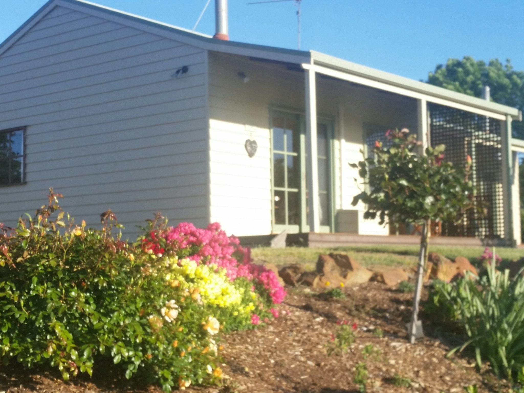 Cream and green weatherboard cottages sit in their own cottage garden in the side of a hill.