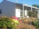 Cream and green weatherboard cottages sit in their own cottage garden in the side of a hill.