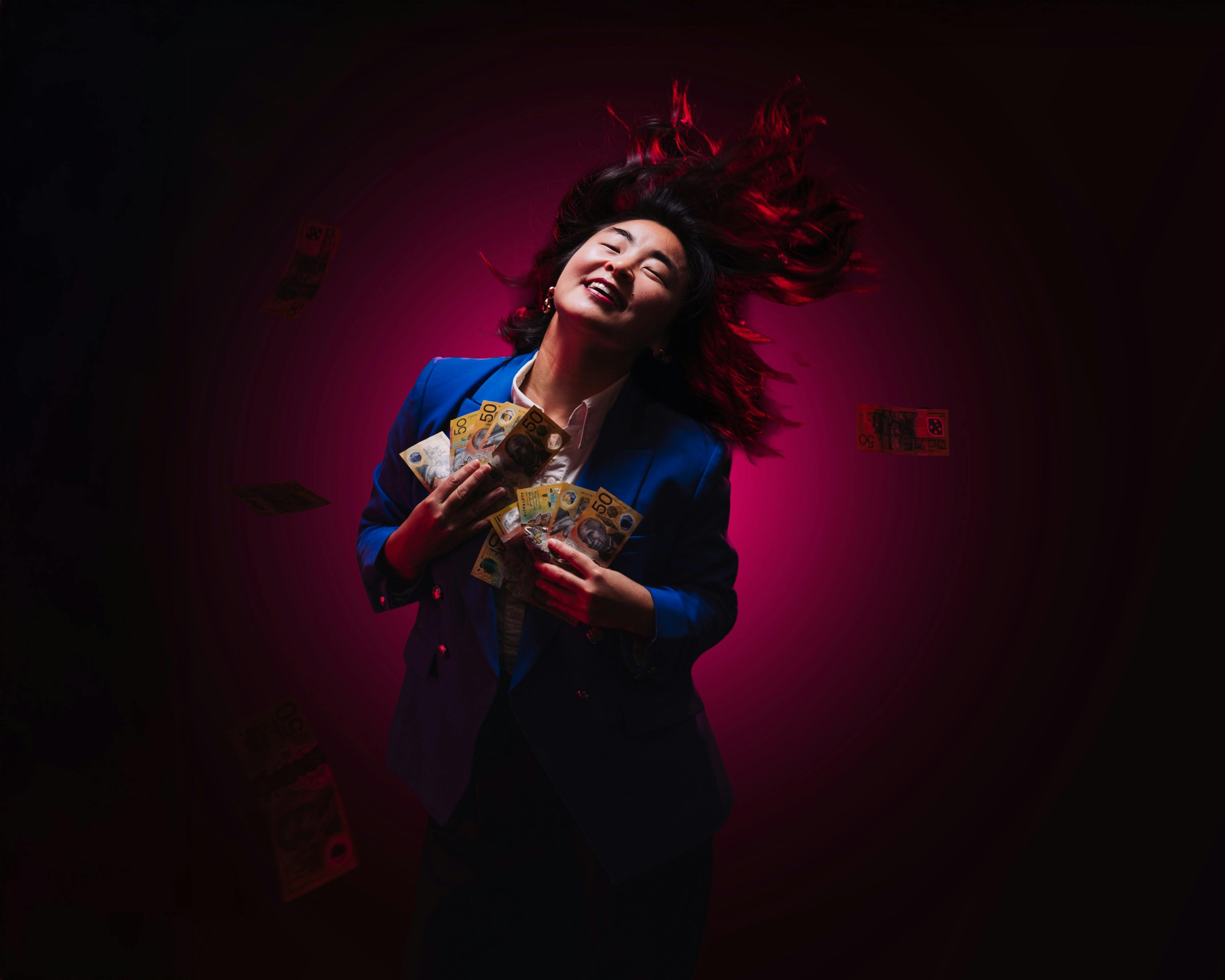 A woman stands with her head flung back, smiling, holding a lot of money