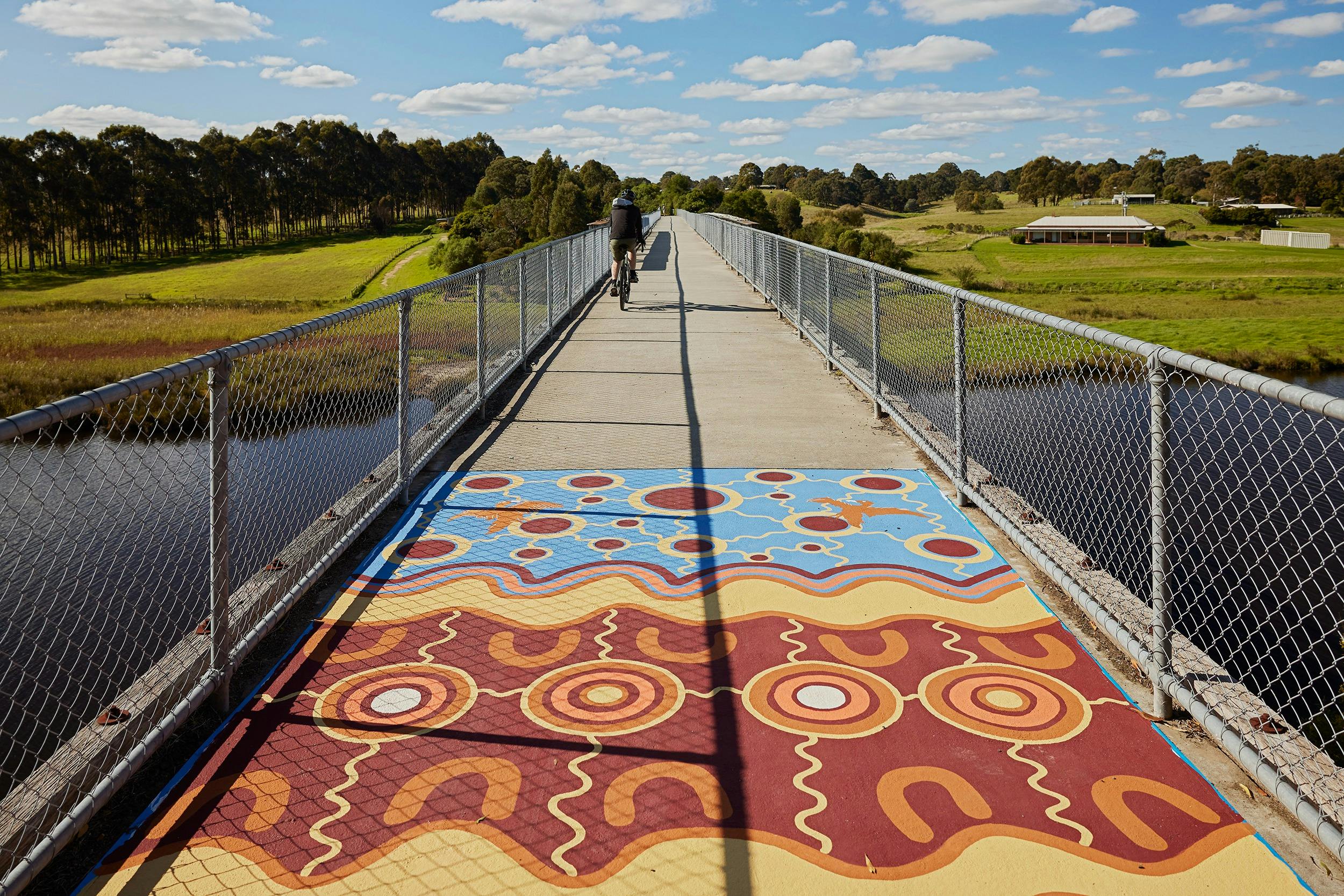 a bridge with a painting made of blue, yellow, orange and maroon with a cyclist on bicycle