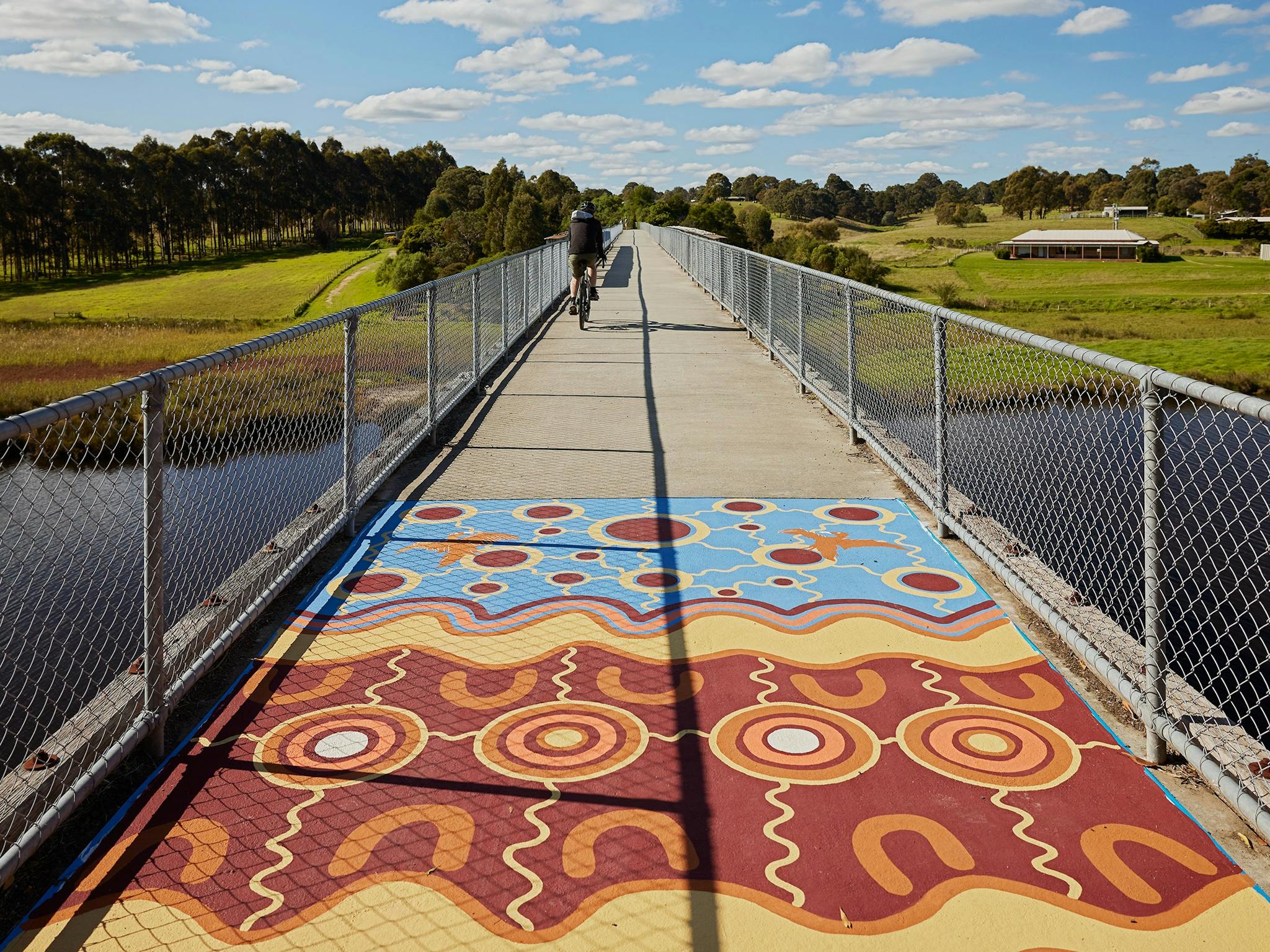 a bridge with a painting made of blue, yellow, orange and maroon with a cyclist on bicycle