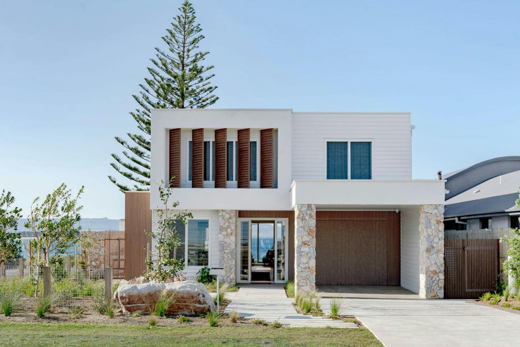 Image of the frony facade of home. With manicured lawns. Backdrop of waterfront location.
