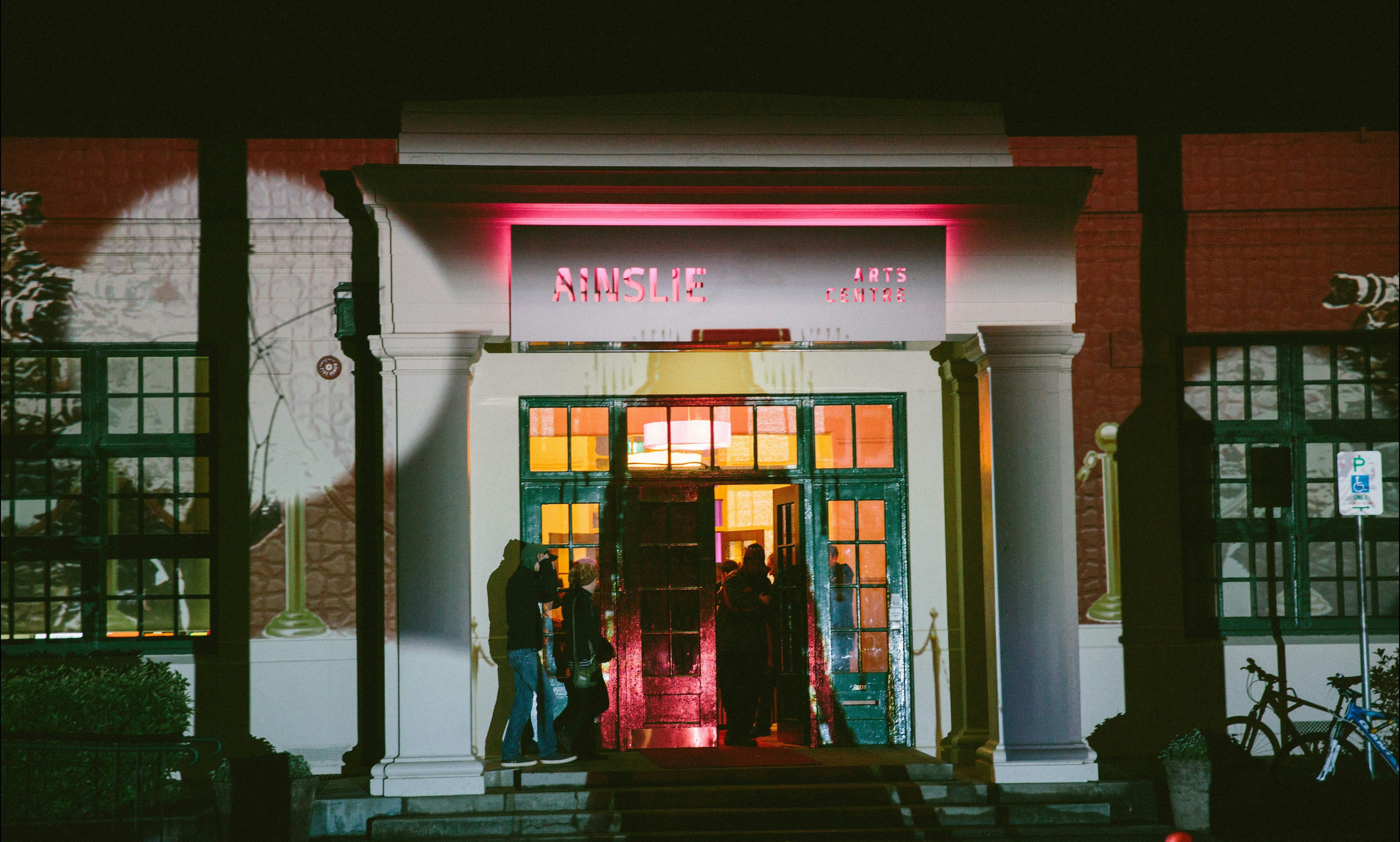 The front facade of the Ainslie Arts Centre, lit up with projected lights and shapes.