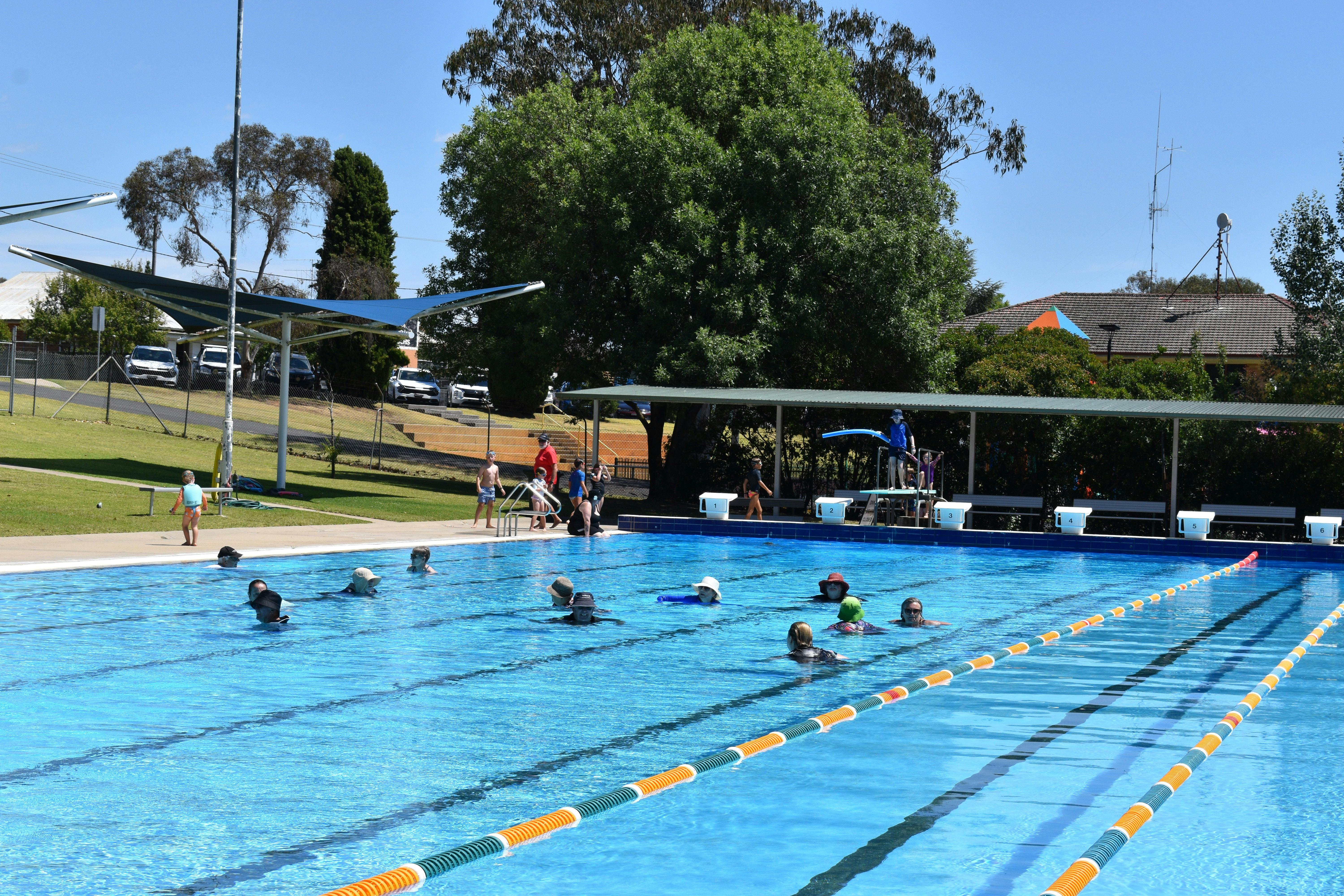 People swimming at the pool. On the far side there are diving boards.