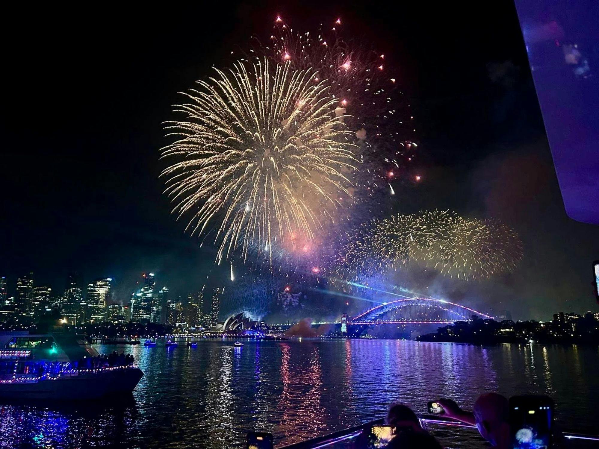 Guests photographing New Year's Eve midnight fireworks from a boat deck over Sydney Harbour