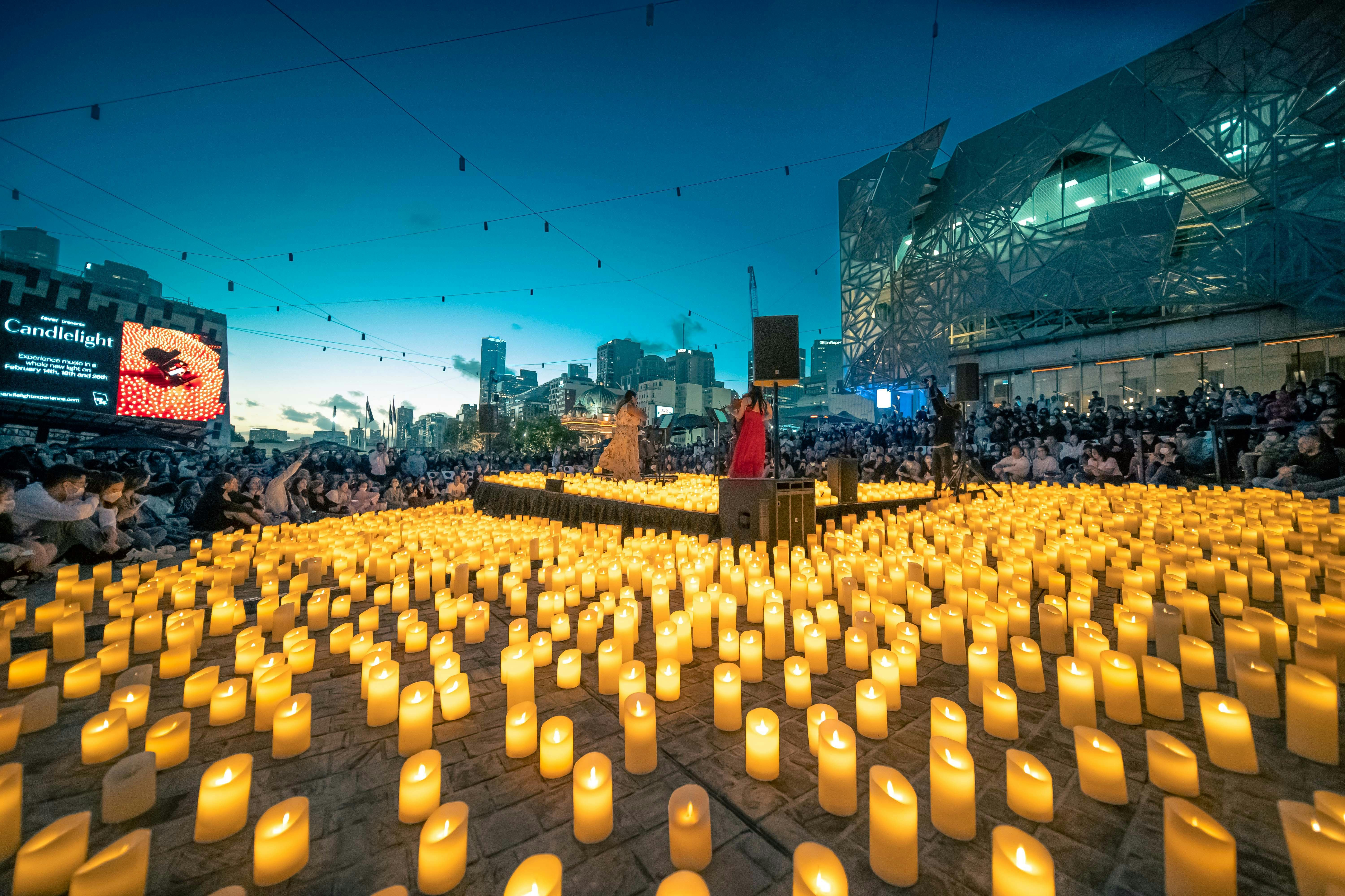 Thousands of candles surround a group of musicians, surrounded by hundreds of spectators.