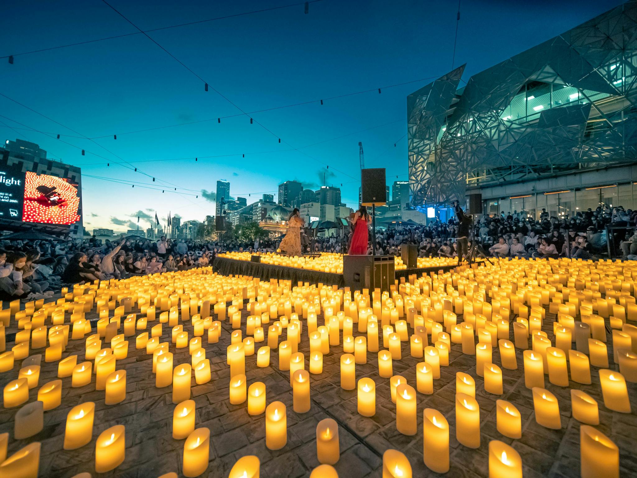 Thousands of candles surround a group of musicians, surrounded by hundreds of spectators.