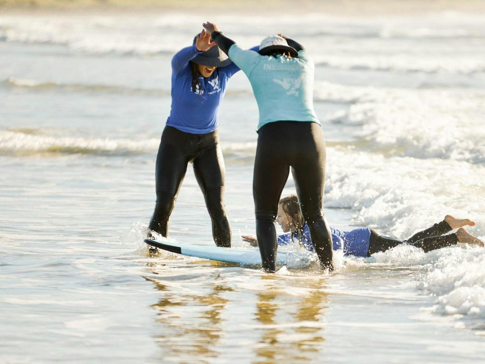 Instructors making tunnel with arms as kid surfs on tummy through