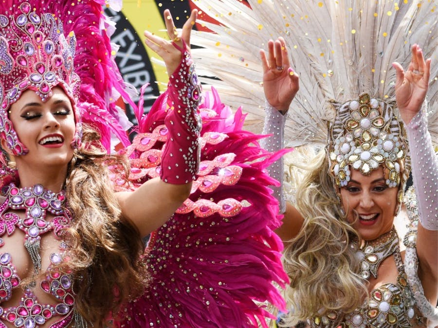 Dancers in jewelled pink and silver costumes with feathers, holding their hands up while smiling