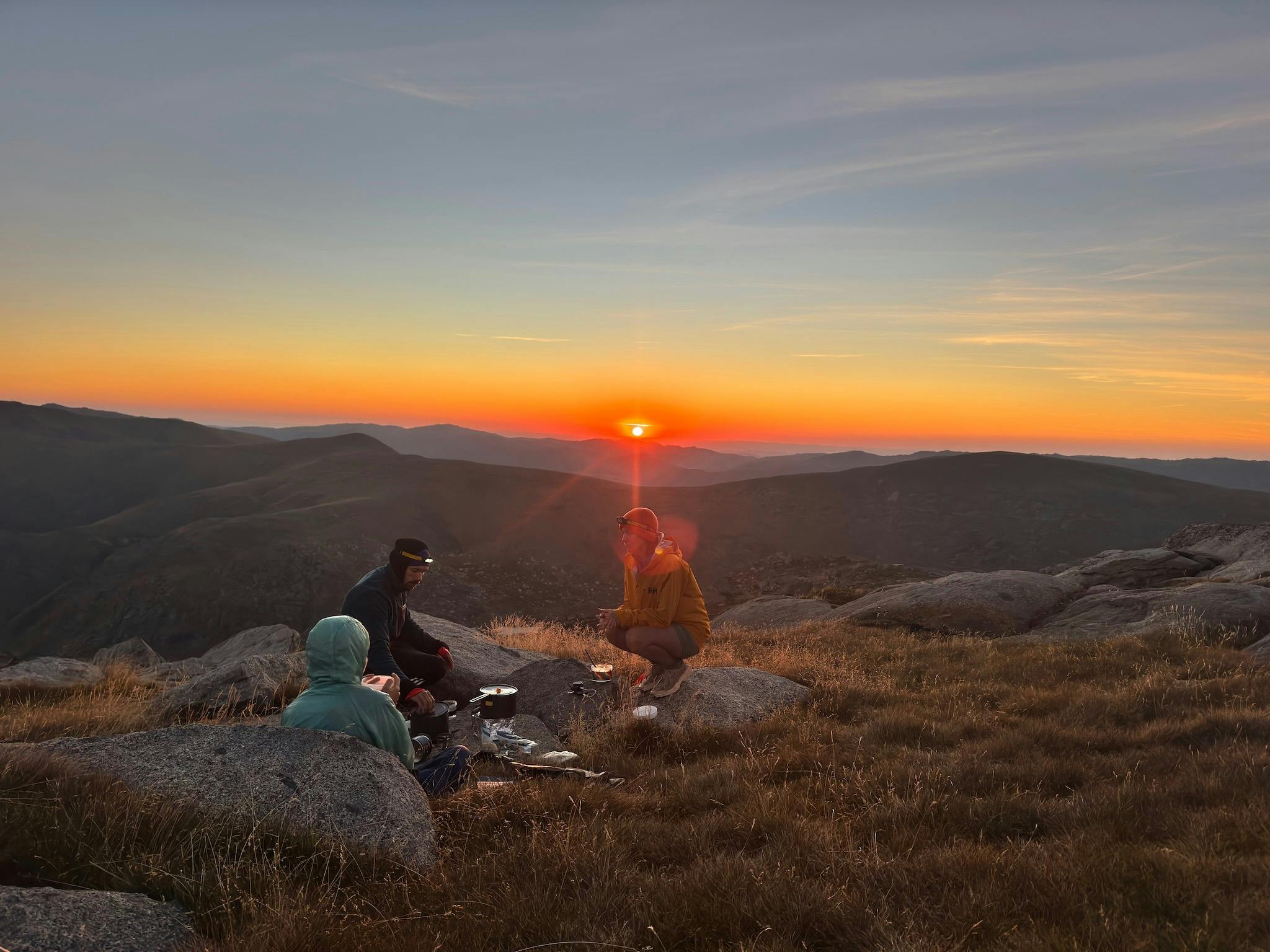 Three hikers in the mountains looking at the sunset