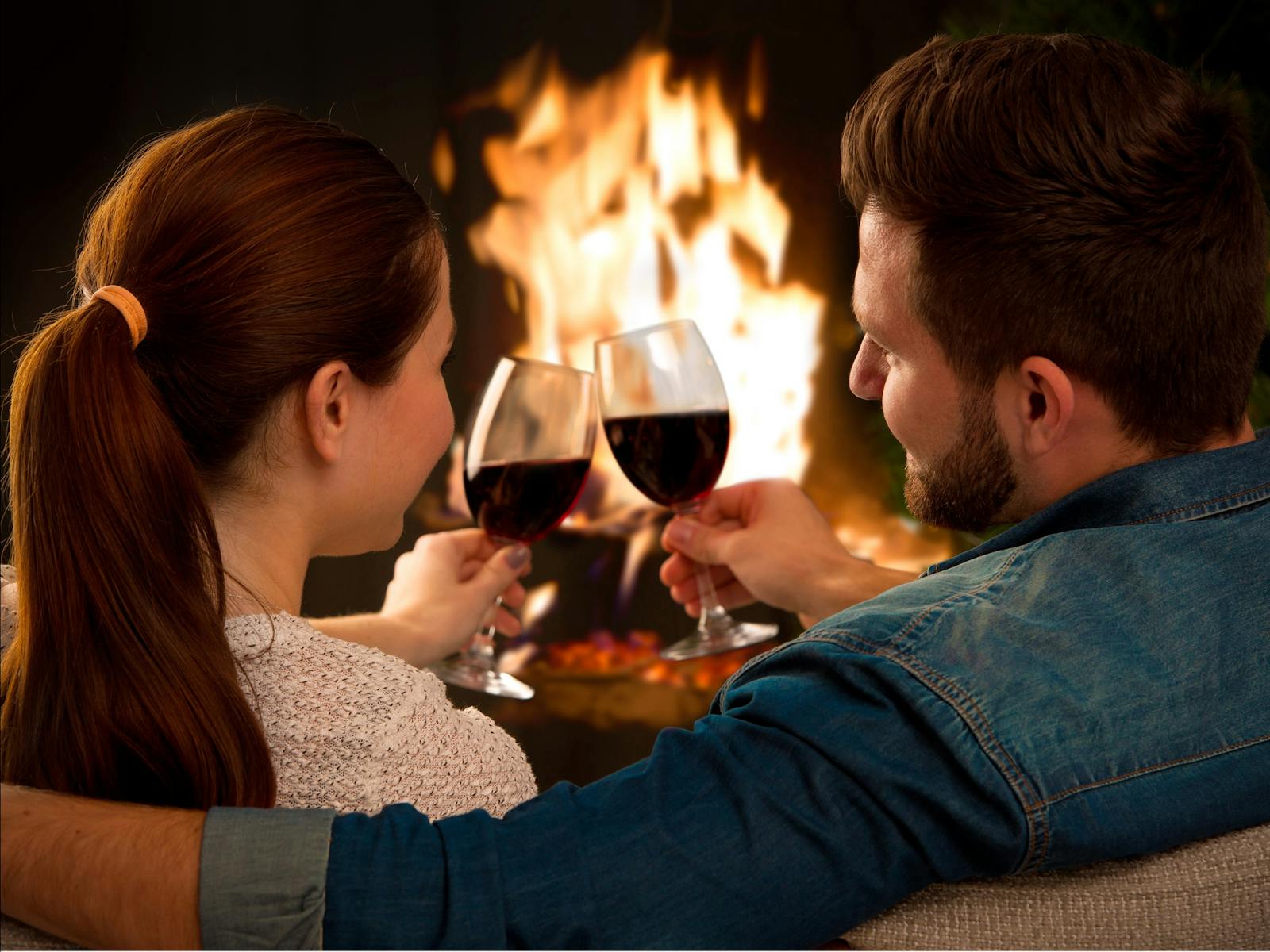 A couple enjoy red wine by the fire