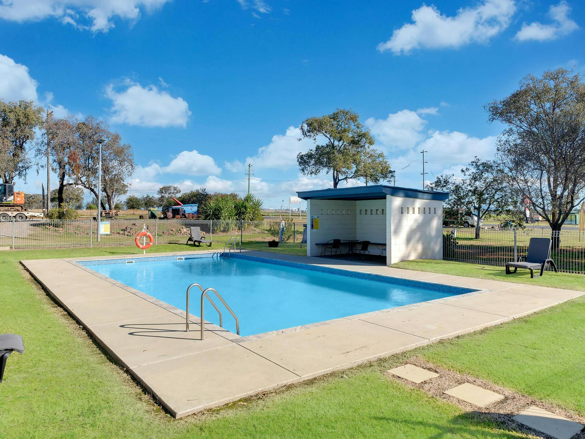 Outdoor swimming pool at Tamworth Holiday Park with shaded seating area, surrounded by grass and a s