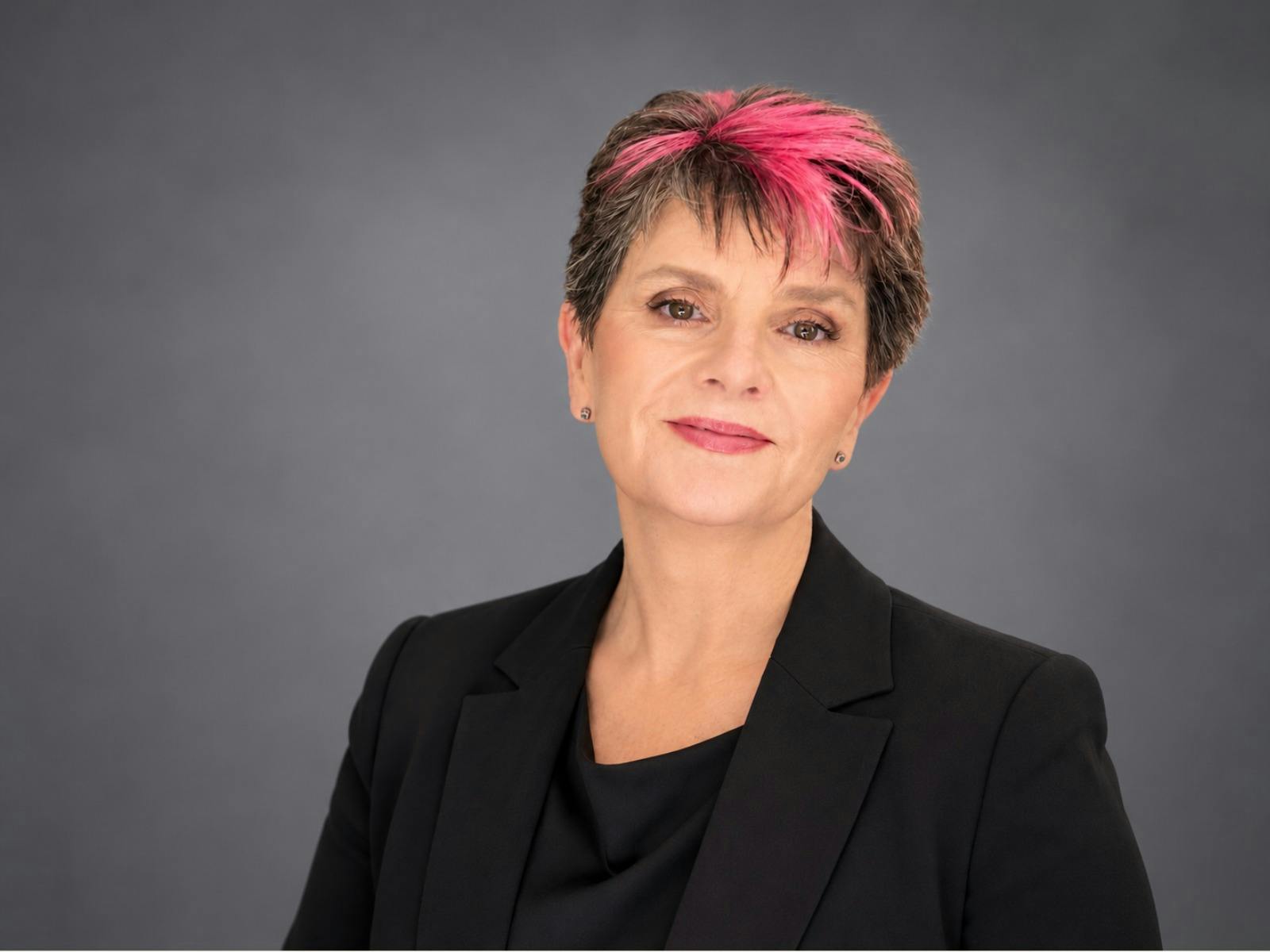 Portrait of Karen Baldwin, a woman with short dark hair with pink highlights, smiling and wearing a