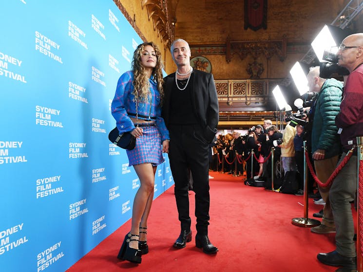 A man and a woman stand stand on the red carpet in front of the Sydney Film Festival media wall