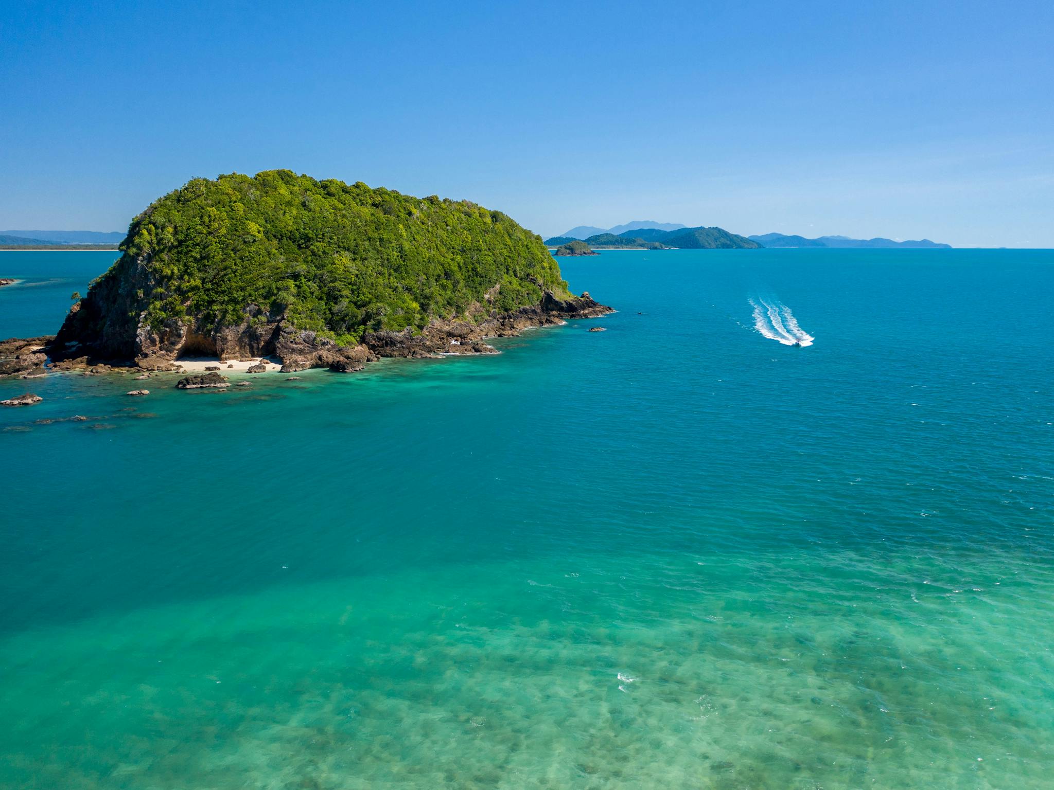 A boat cruises across tropical seas next to an island