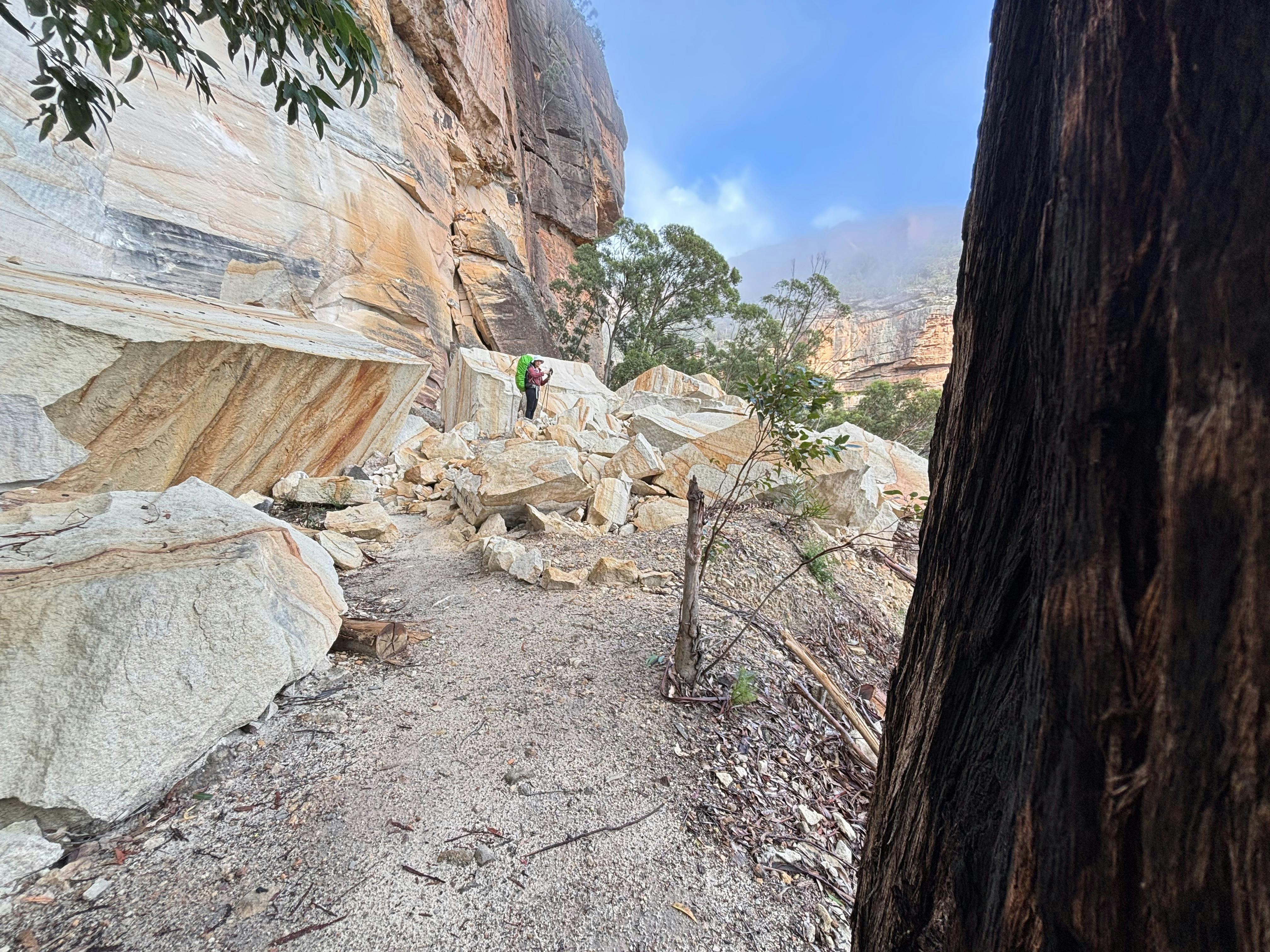A woman wearing a checked shirt stands next to several huge sandstone blocks on the disused railway